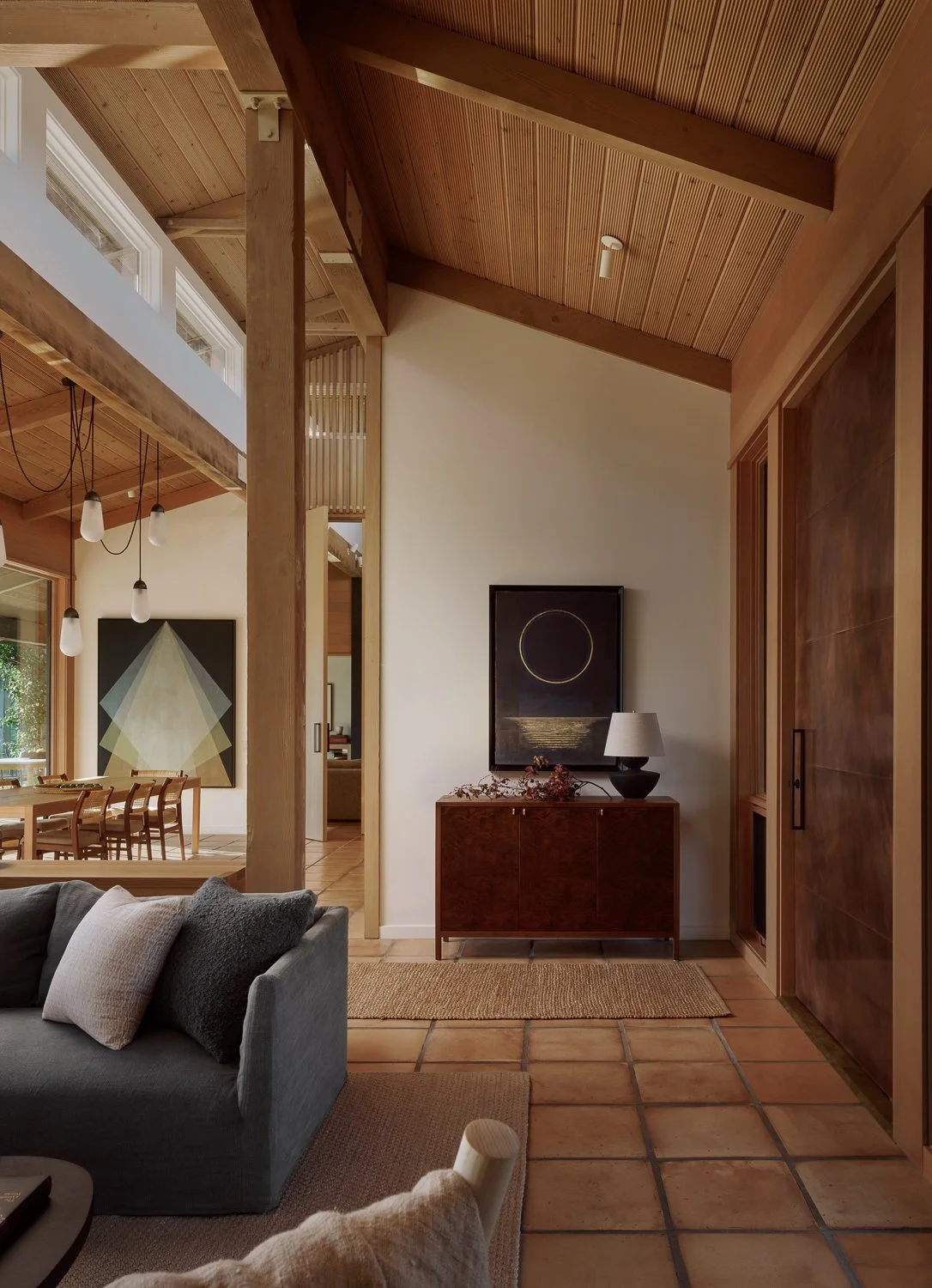 Foyer of a Sonoma, California home featuring a custom walnut credenza, Gessho Moon by Ken Matsubara, a sculptural copper entry door, and a sightline to the dining room beyond.