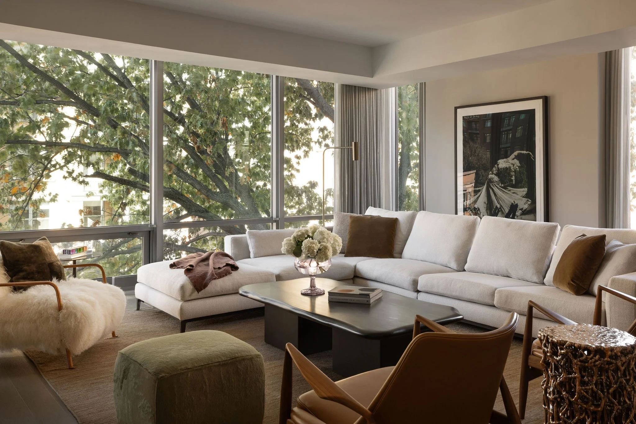 Living room of a Georgetown condo designed by Laura Roberts Design featuring a Minotti sectional, a large black-and-white photograph of Ruth St. Denis as Radha, sculptural seating, and contemporary furnishings framed by a large window and mature tree