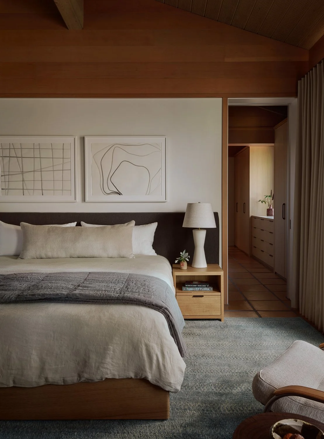 Custom white oak bed upholstered in Holland & Sherry fabric defining this Sonoma bedroom, with sculptural plaster bedside lamps, minimalist artwork, and a view into the white oak millwork of the custom closet.