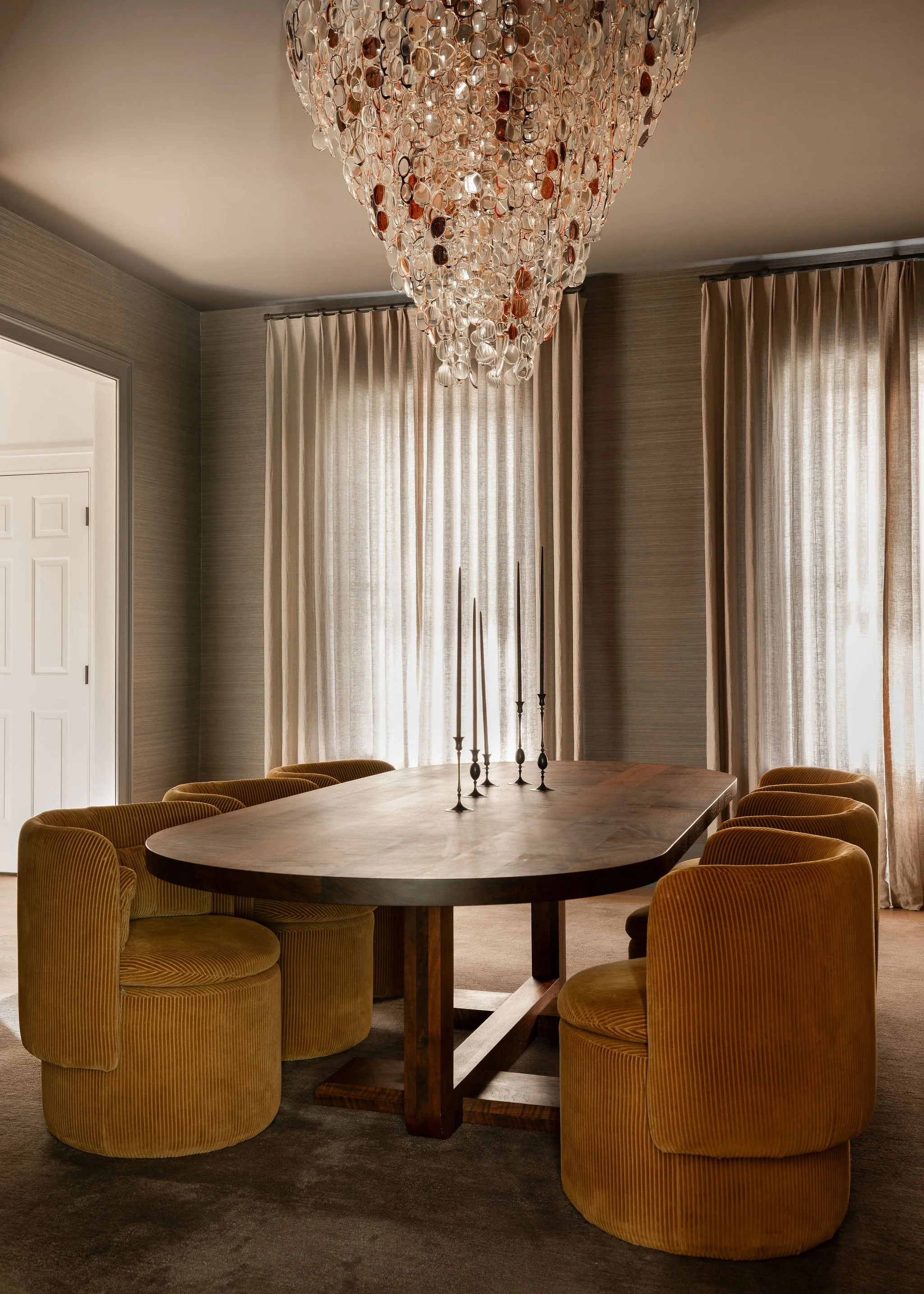 Dining room in a McLean, VA home with a custom walnut dining table featuring a sculptural base, mustard upholstered chairs, and the Spectacle chandelier by Stuart Haygarth, shown against soft sheer window treatments.