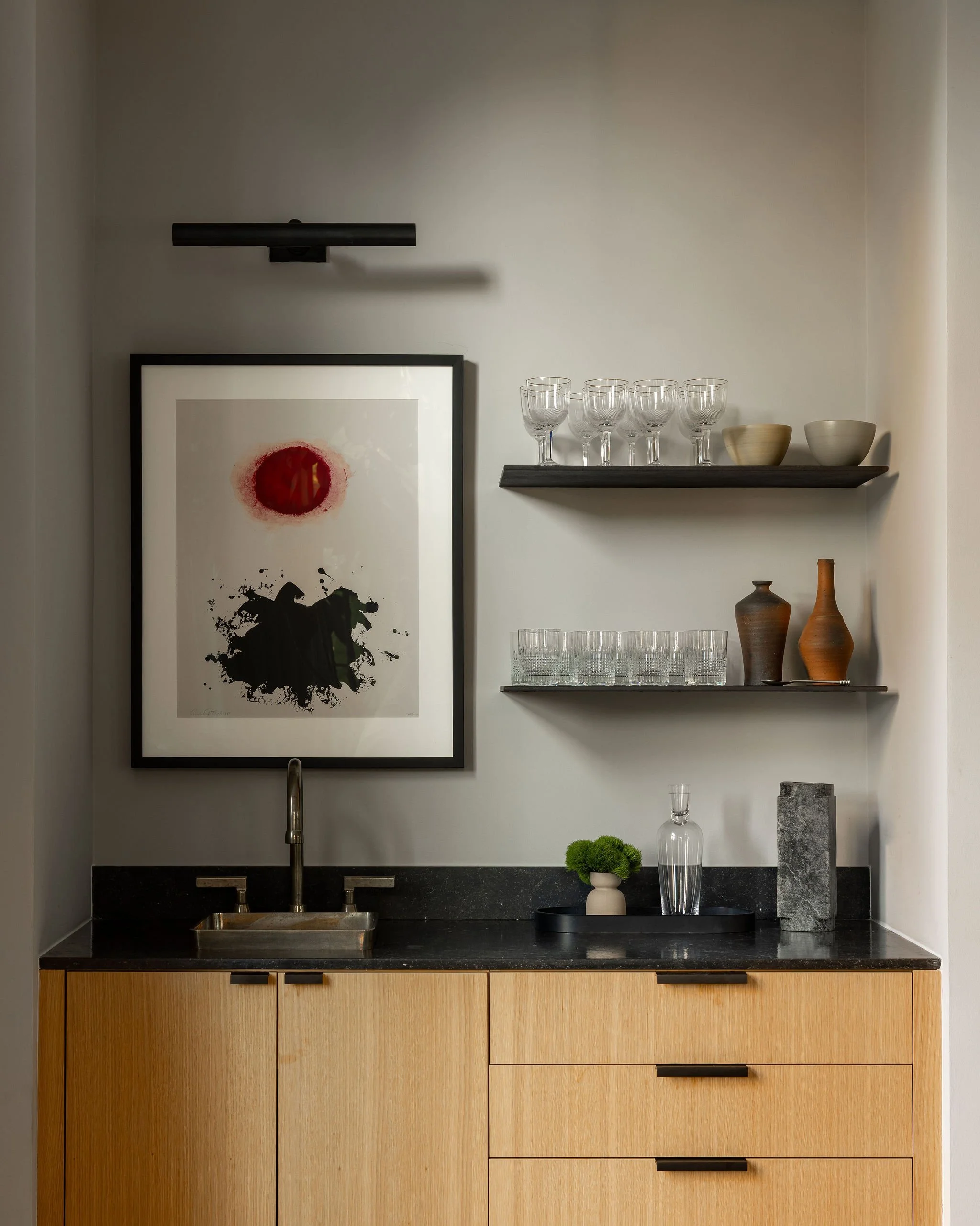 Detail of the renovated living room bar in a McLean, VA home featuring custom white oak cabinetry, a bronze bar sink, open shelving, and a framed Gottlieb print.