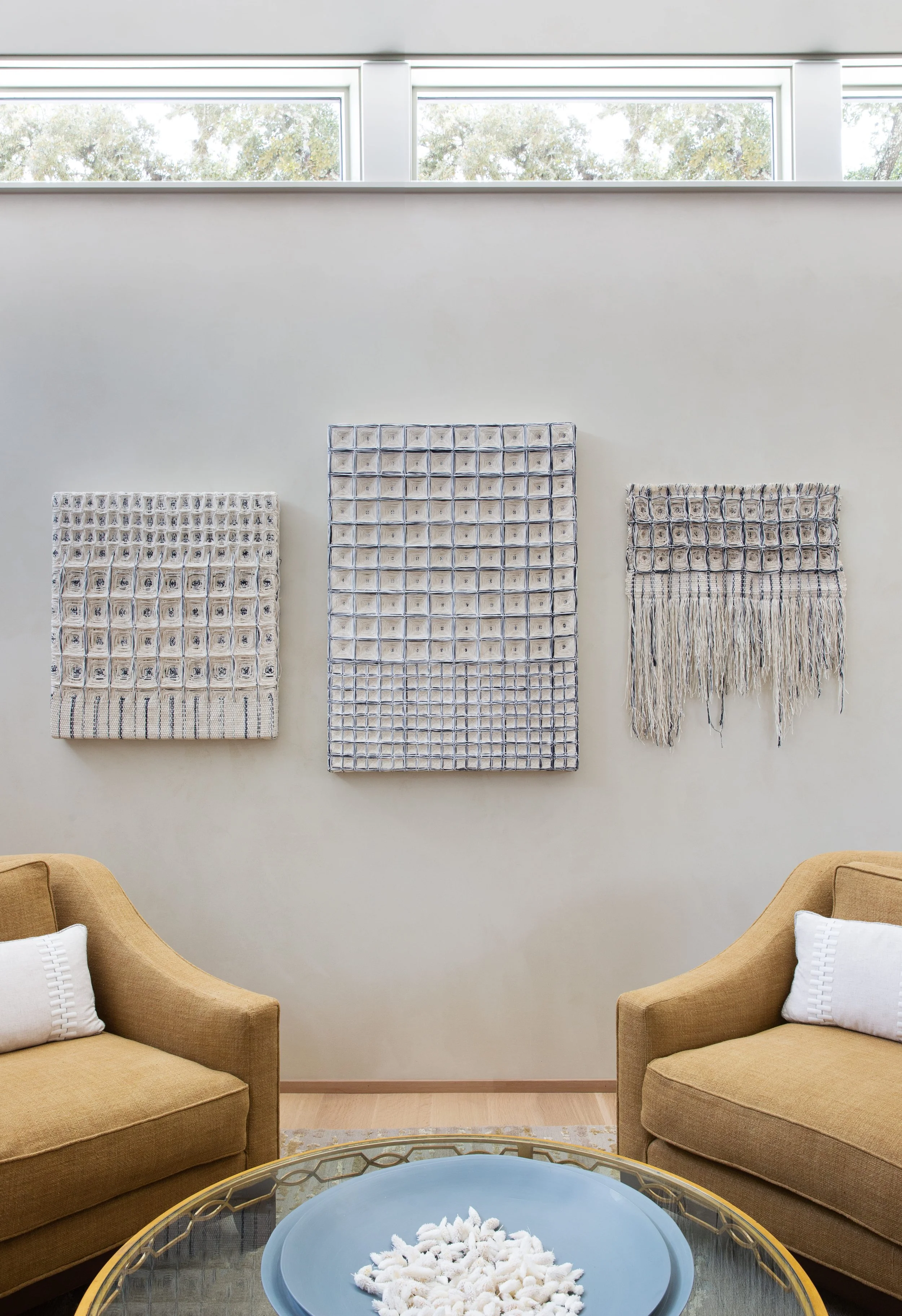 Front sitting room with upholstered lounge chairs and textile wall art by Hiroko Takeda Studio on plaster walls.