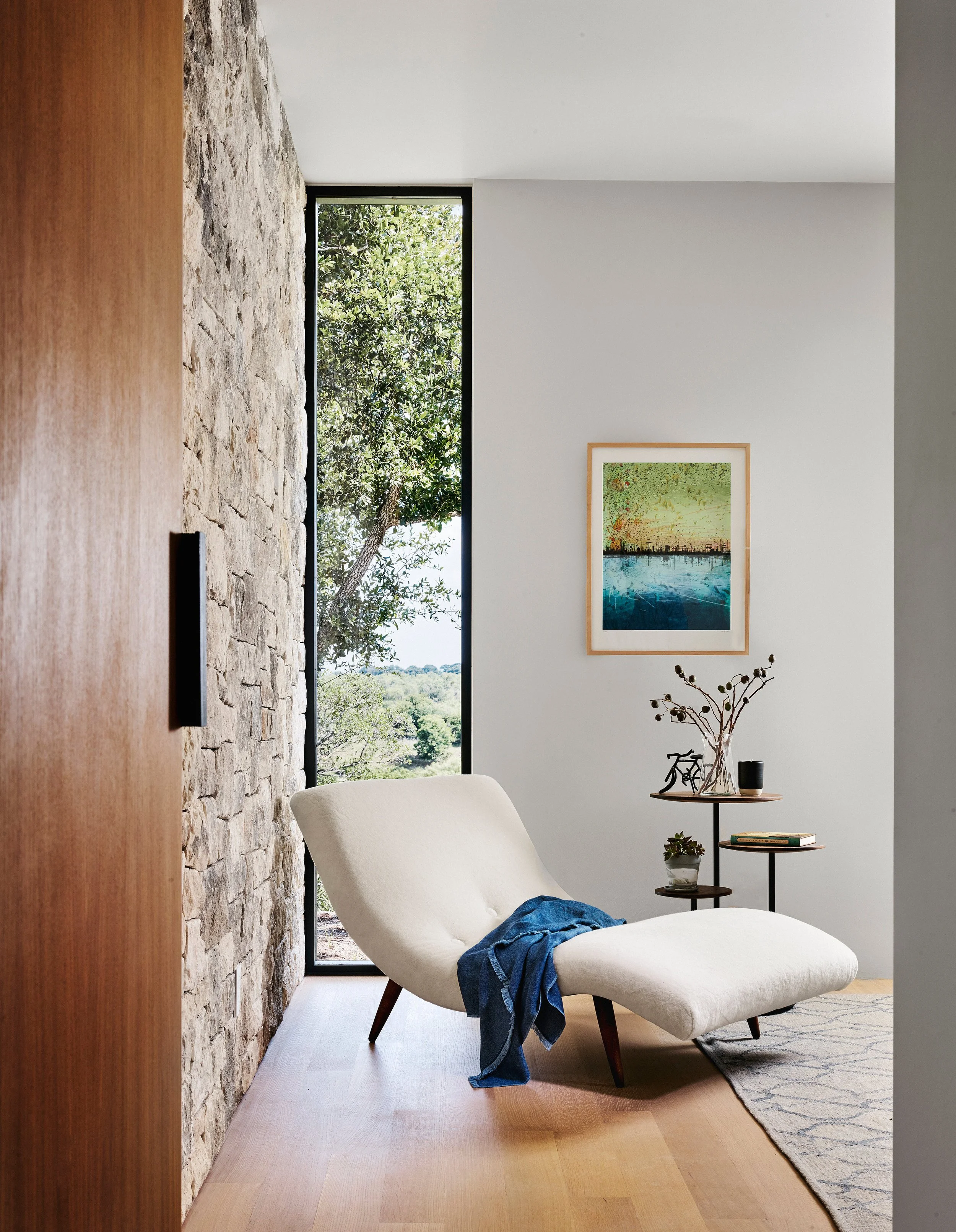 Primary bedroom vignette featuring a vintage chaise lounge set against a Texas limestone wall, with tall white oak doors, natural light, and views to the surrounding Hill Country landscape.
