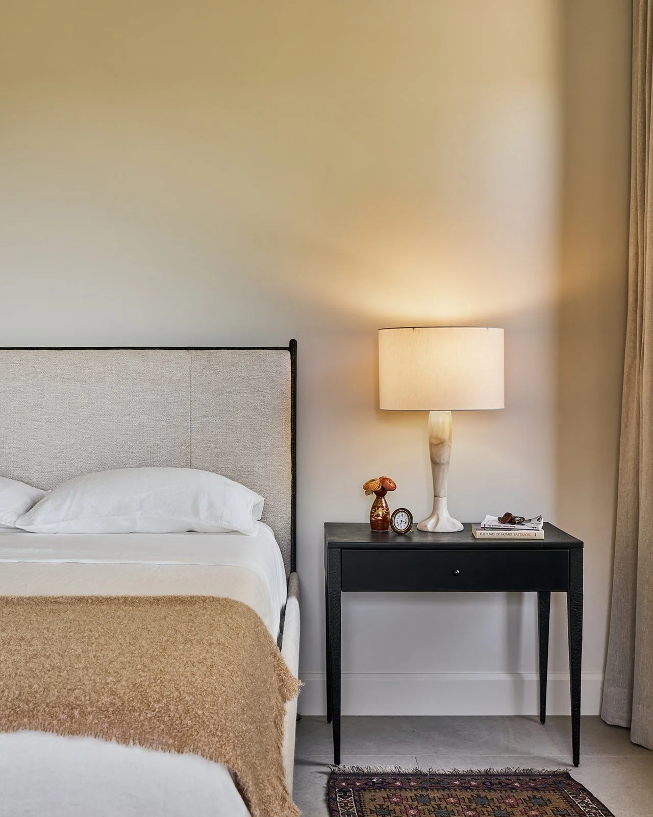 Minimal Austin interior design primary bedroom featuring a Baker McGuire upholstered bed, coordinating nightstand, and vintage alabaster table lamp styled by Laura Roberts Design.