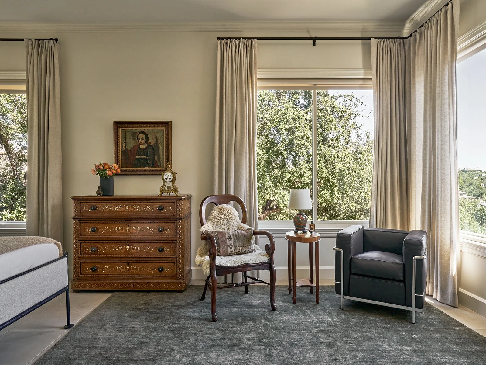 Primary bedroom in an Austin interior design project featuring a solid green linen rug, antique dresser with a vintage Archangel Raphael painting, a classic antique chair, and a Cassina 3 Fauteuil Grand Confort chair styled by Laura Roberts Design.