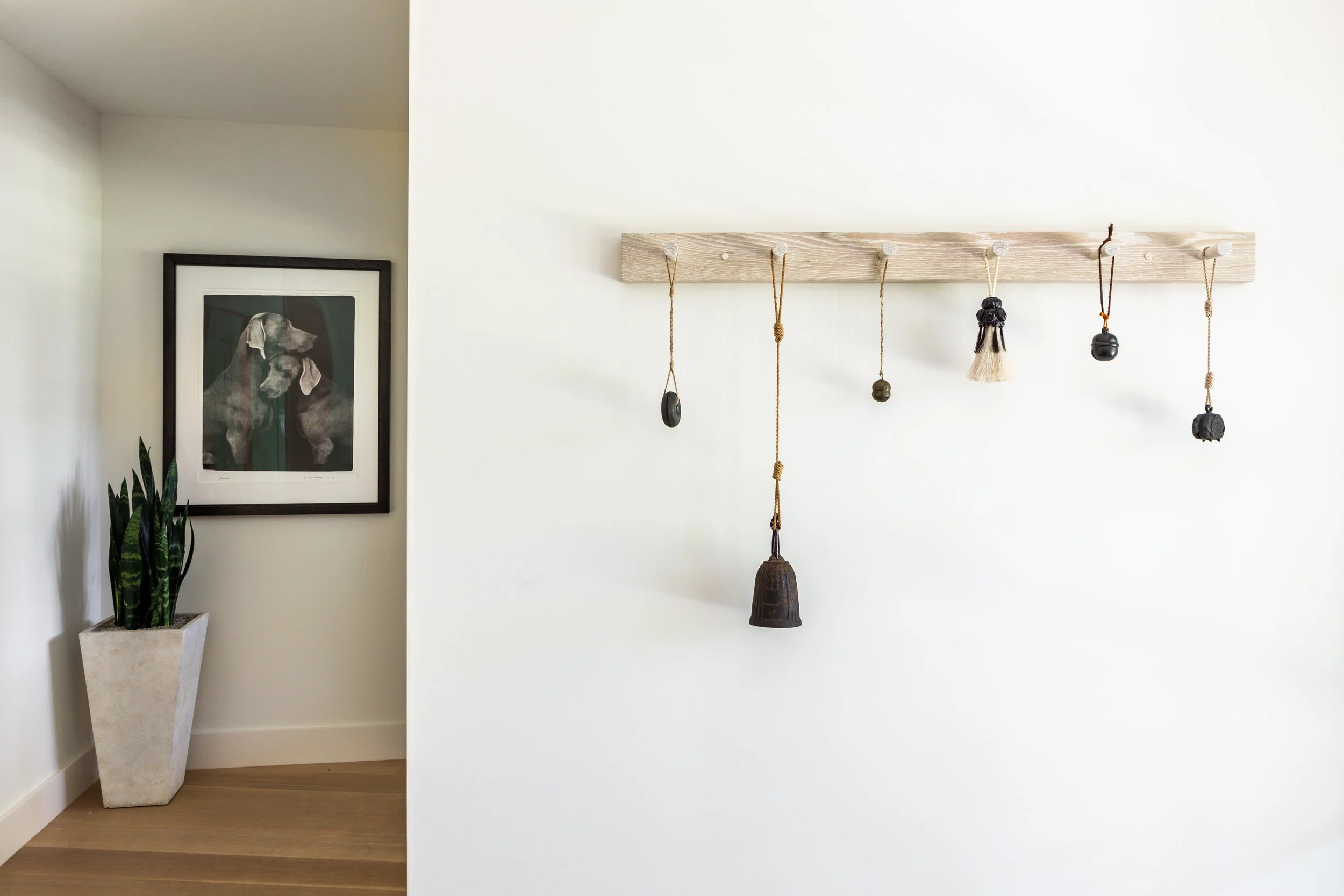Austin home entry art vignette featuring antique Japanese bells on custom wood coat rack and black-and-white dog photograph by William Wegman.