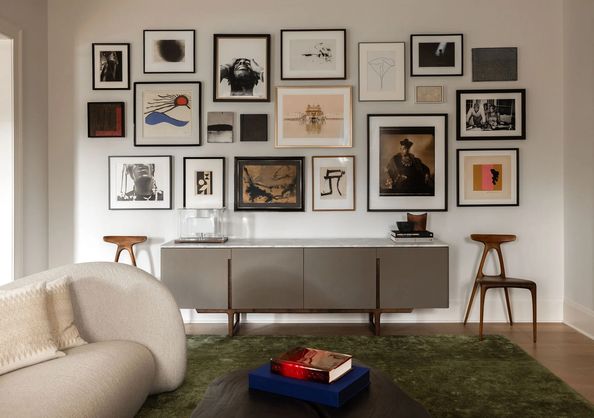 Salon-style gallery wall in a McLean, VA living room featuring works by Calder, portraits of Snoop Dogg and Queen Latifah, the Golden Temple, and abstract art above a leather-fronted Cassina credenza with Alpha walnut chairs.