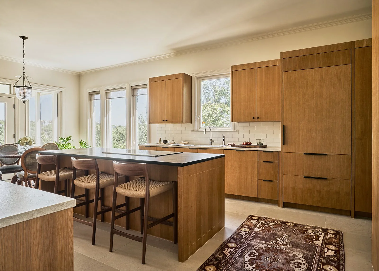 Austin kitchen design blending warm white oak cabinetry with a soapstone island countertop, vintage rug, and mid-century counter stools creating a modern yet inviting space styled by Laura Roberts Design.