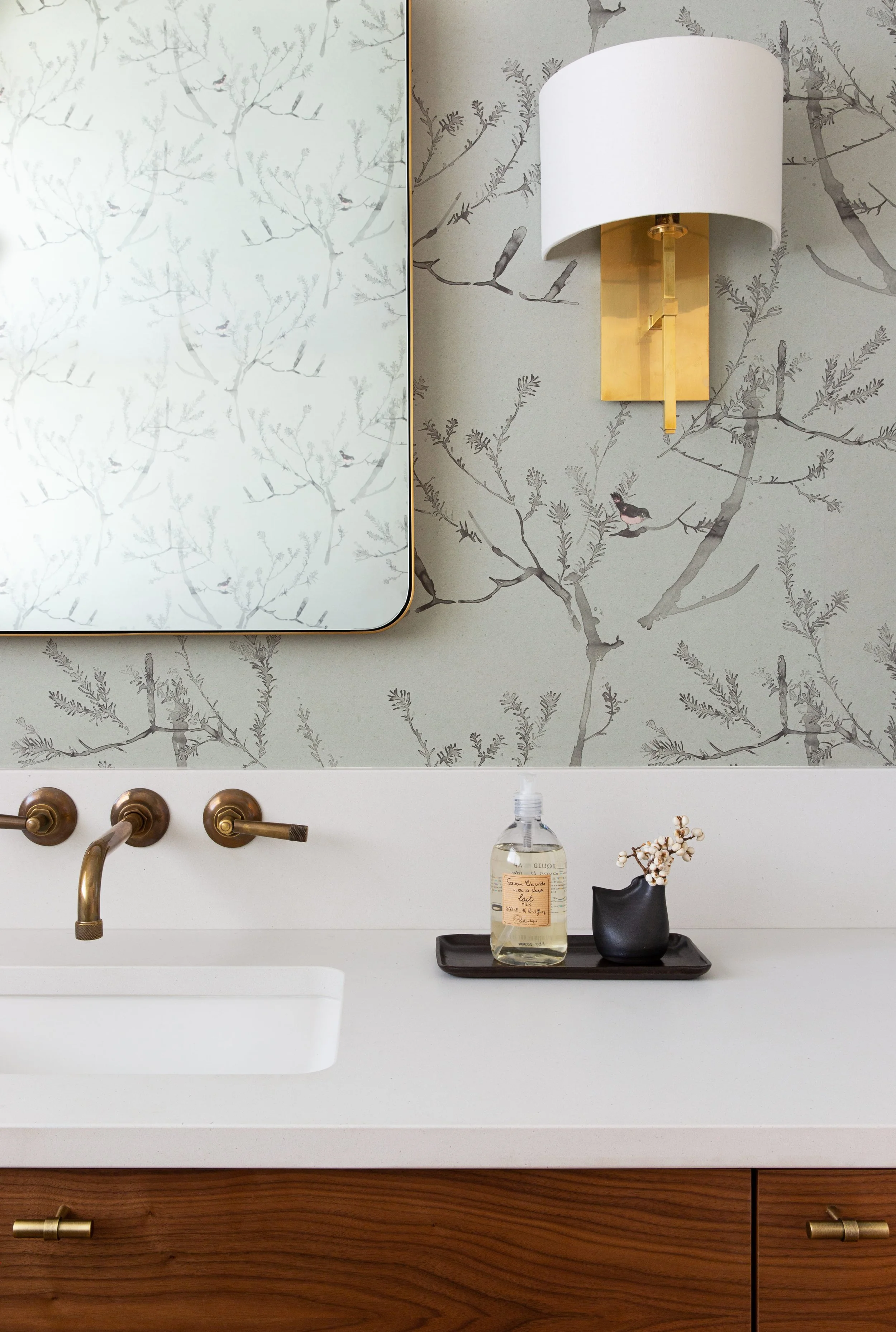 Powder bathroom with Quercus & Co. bird wallpaper, antique brass wall-mounted faucet, custom vanity, and nature-inspired decor.