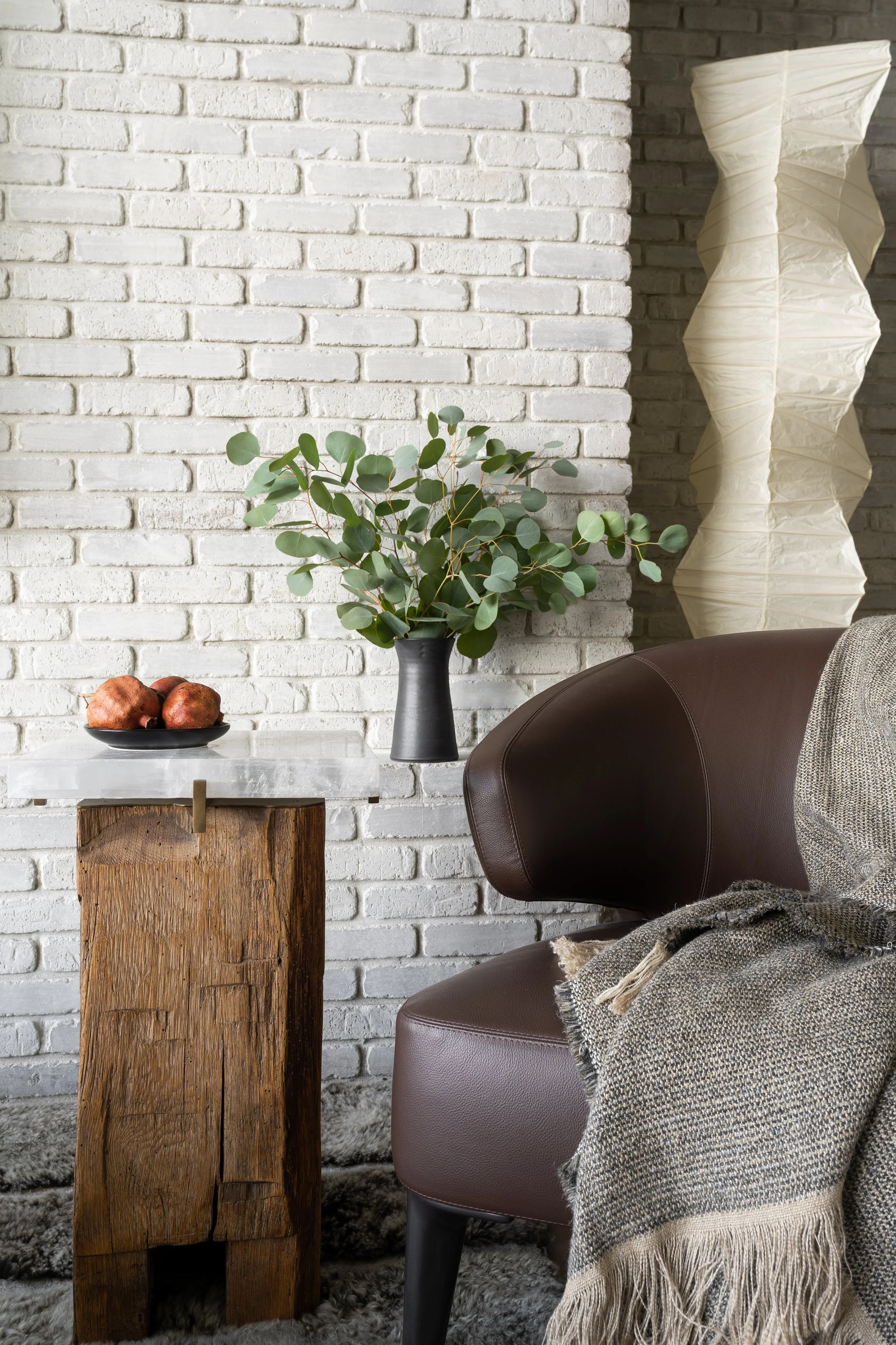 Detail of Minotti leather lounge chair paired with a Noguchi floor lamp and selenite side table from Blakman Cruz against a limewashed brick wall.