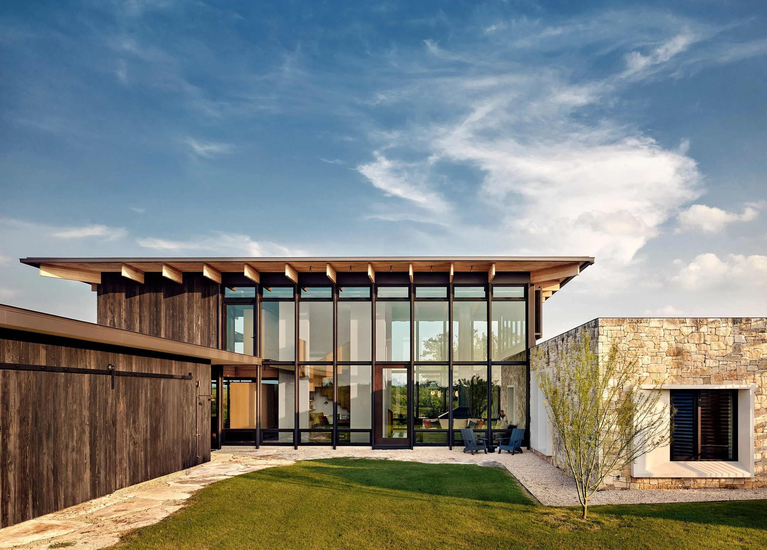 Modern Hill Country home on the Llano River designed by Laura Roberts Design, featuring Texas limestone, expansive glass walls, and shou sugi ban wood siding integrated into the natural landscape.