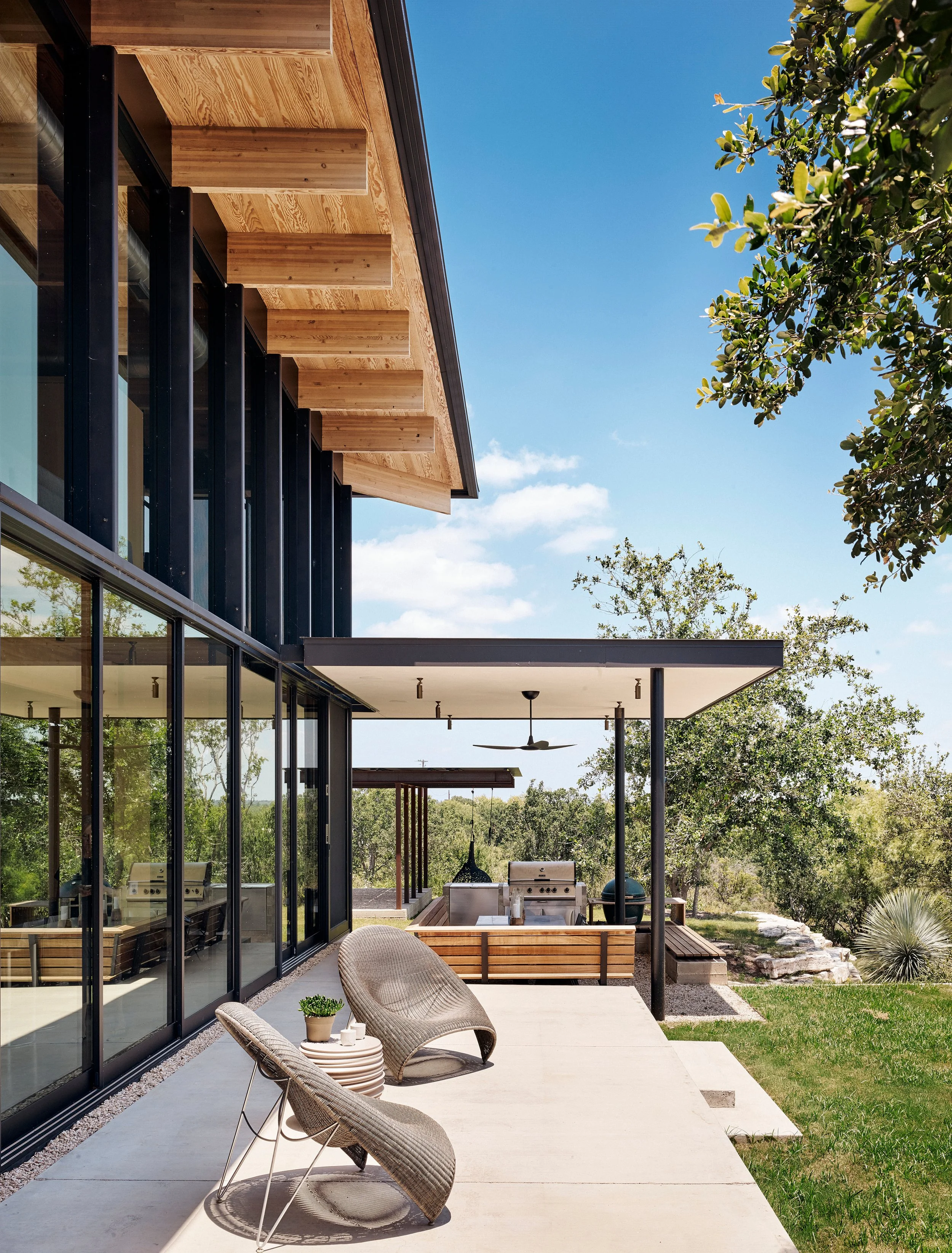 Exterior terrace of a modern Hill Country home with sculptural lounge chairs positioned to overlook the Llano River and surrounding landscape.