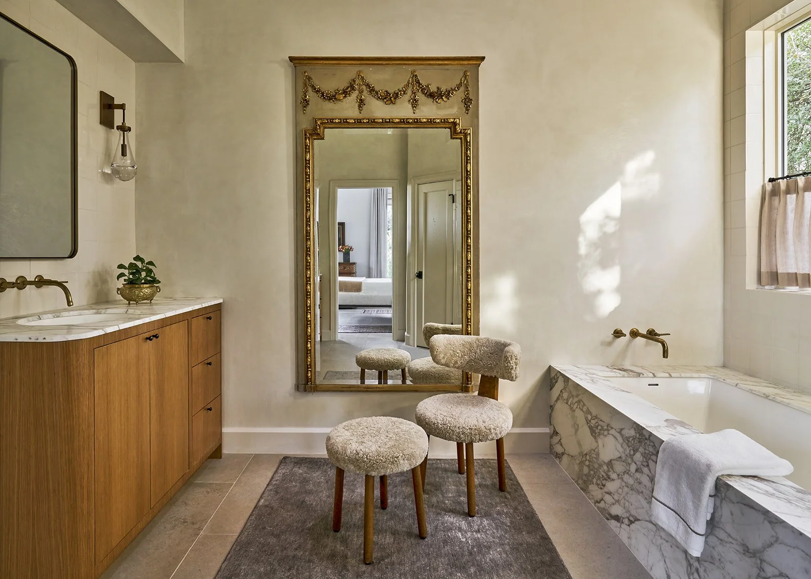 Primary bathroom in an Austin interior design project featuring a marble tub surround, Leuders limestone floors, white oak cabinetry, and an antique Trumeau mirror styled by Laura Roberts Design.