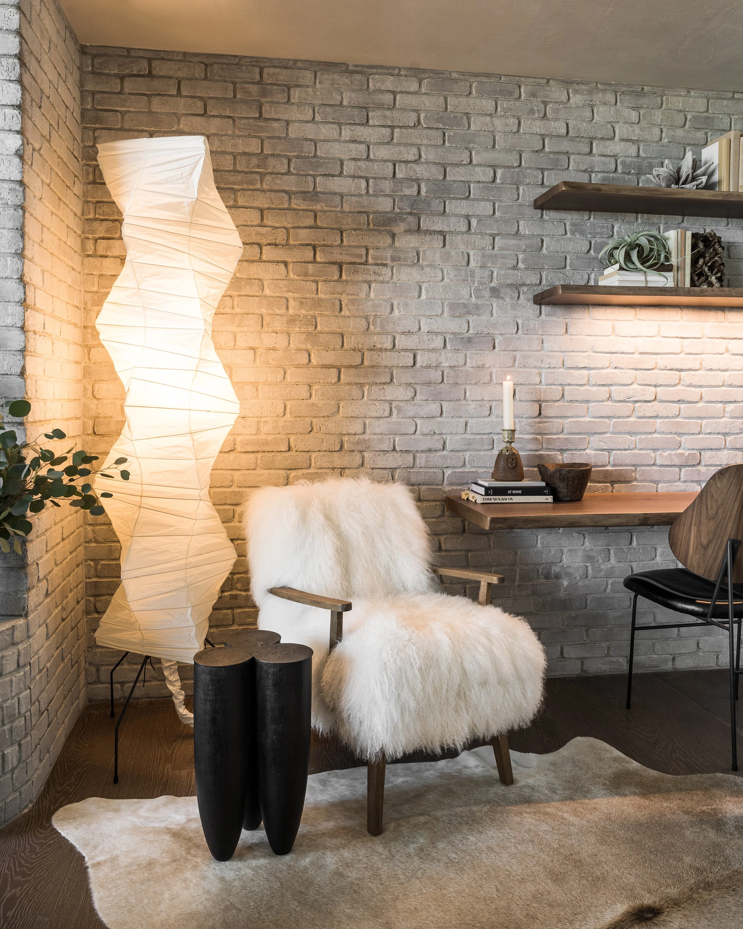 Home office lounge featuring a custom live-edge cantilevered walnut desk, sculptural lounge chair, Noguchi floor lamp, wood side table, and limewashed brick wall.