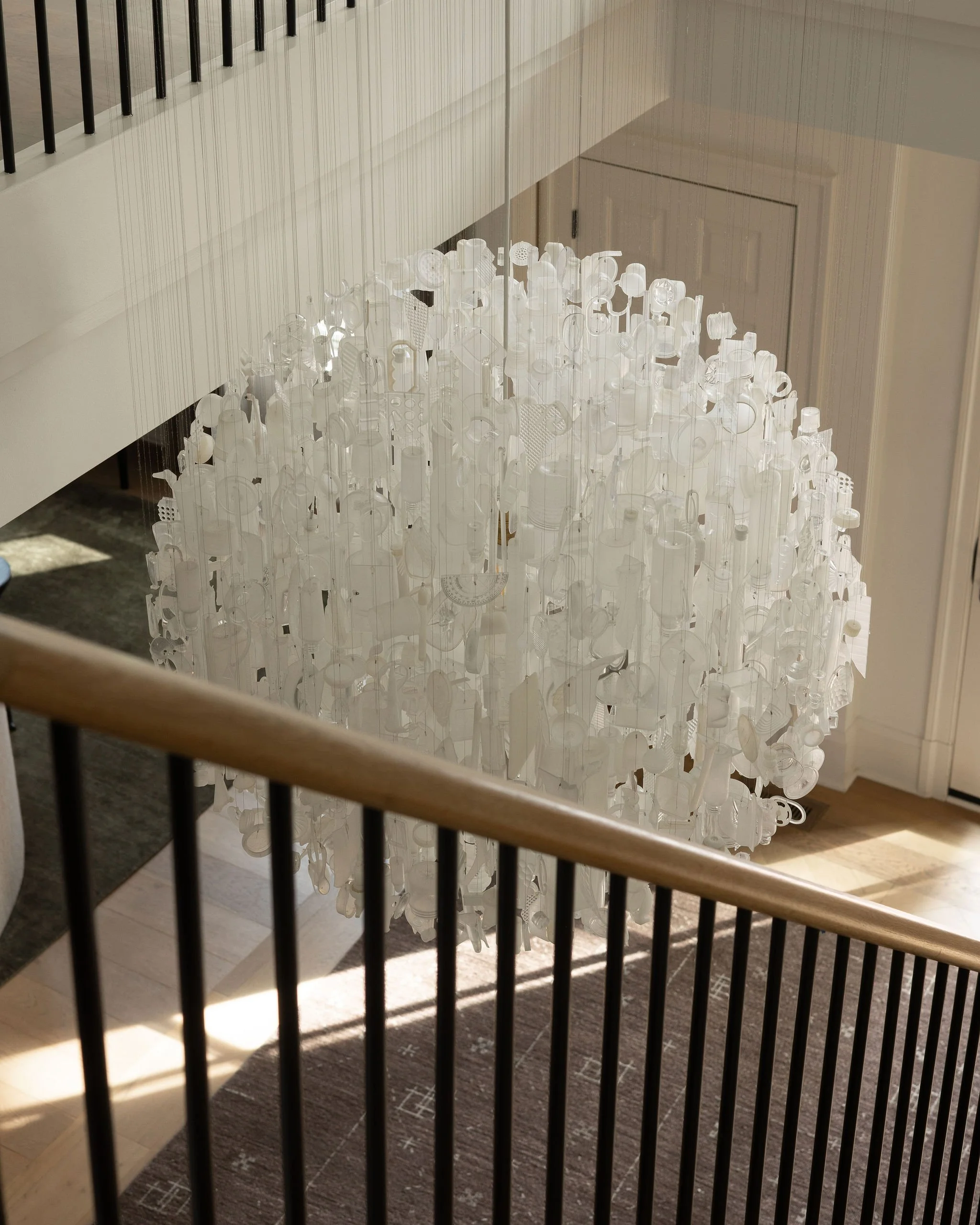 Detail of the custom oak stair handrail and the Tide chandelier by Stuart Haygarth, crafted from found ocean plastic, in a renovated McLean, VA home.