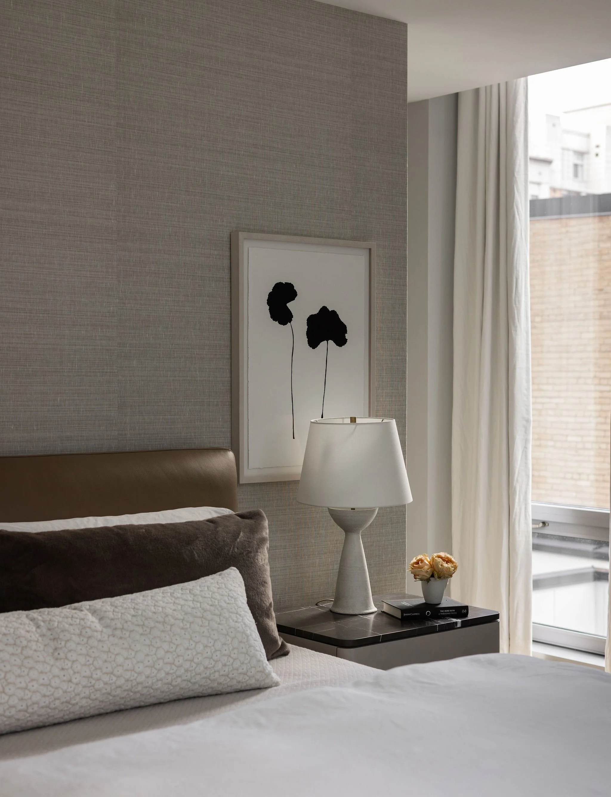 Peaceful primary bedroom in a Georgetown condo by Austin interior designer Laura Roberts Design, featuring a Minotti bed, plaster table lamp, commissioned Mia Carameros painting, Holly Hunt grasscloth wallpaper, and layered luxury bedding.