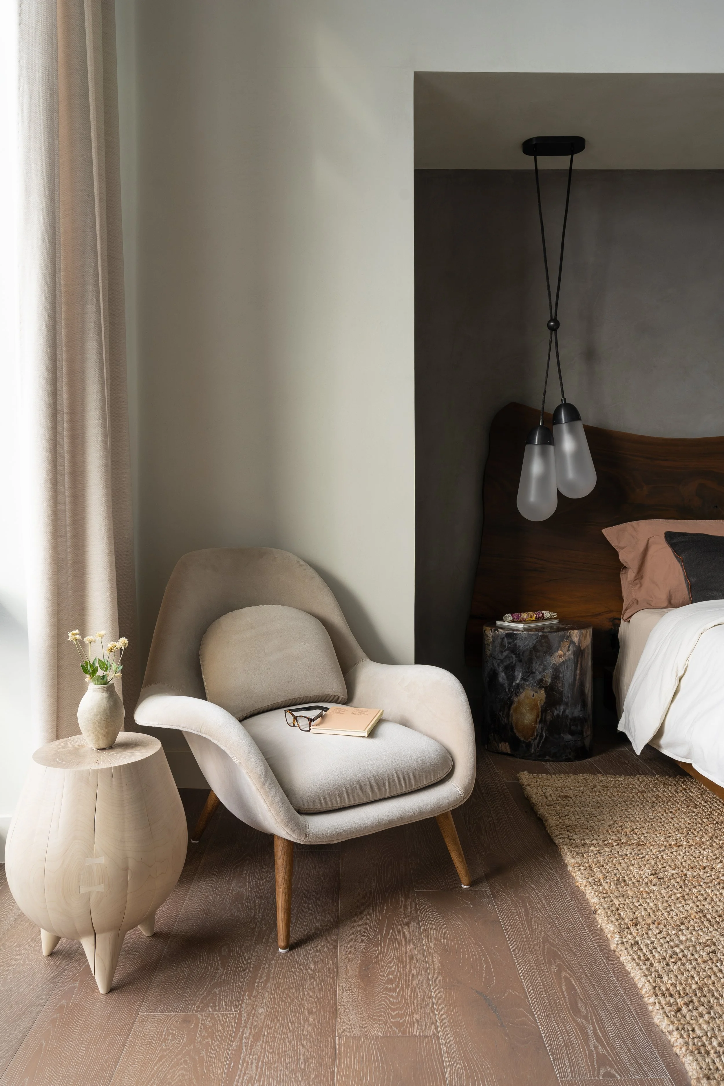 Primary bedroom sitting area by a full-height window with a sculptural lounge chair and bleached wood side table by Kieran Kinsella, layered in soft neutral tones.
