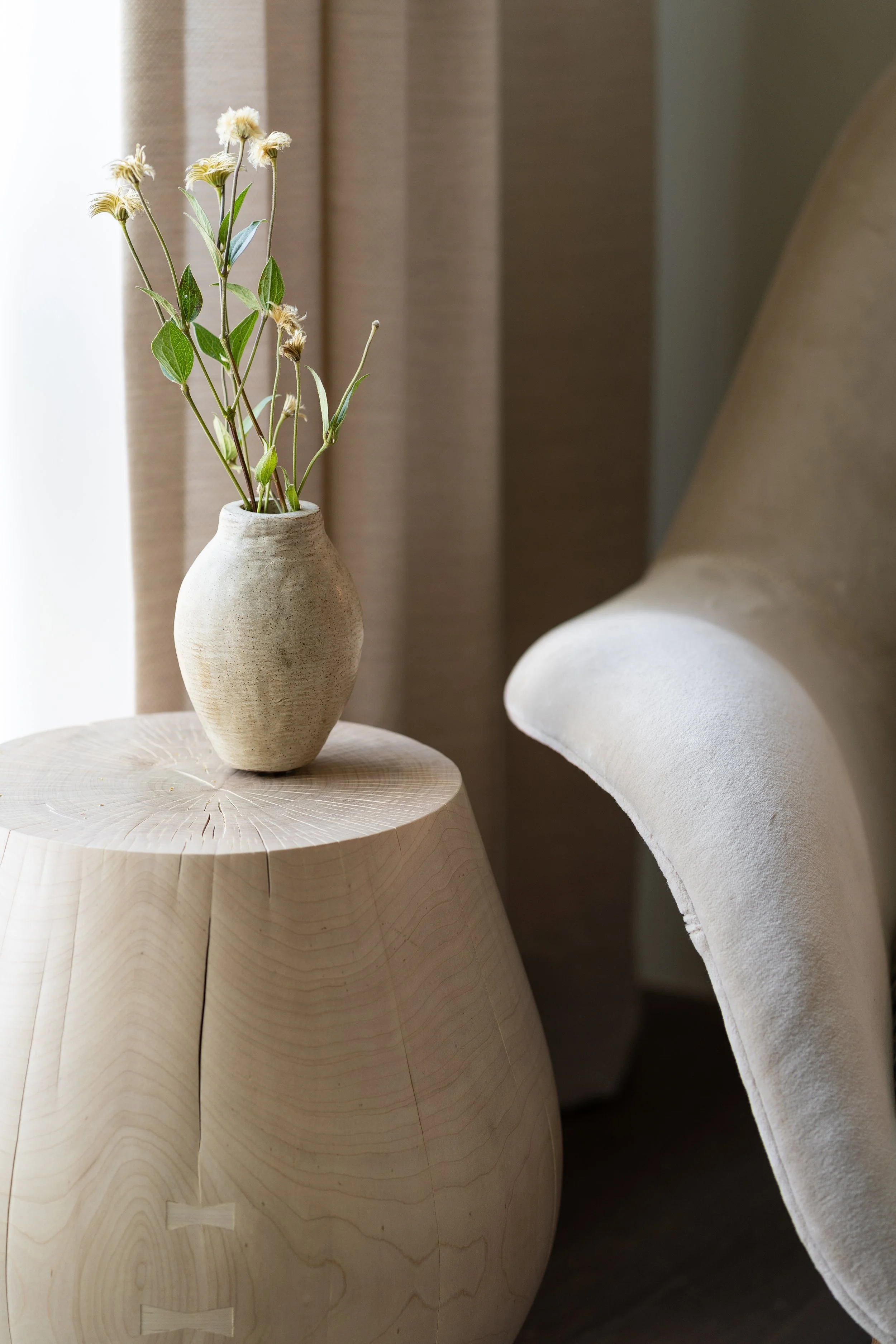Close-up of sculptural lounge chair paired with a bleached wood side table, highlighting soft curves and natural textures in the primary bedroom.