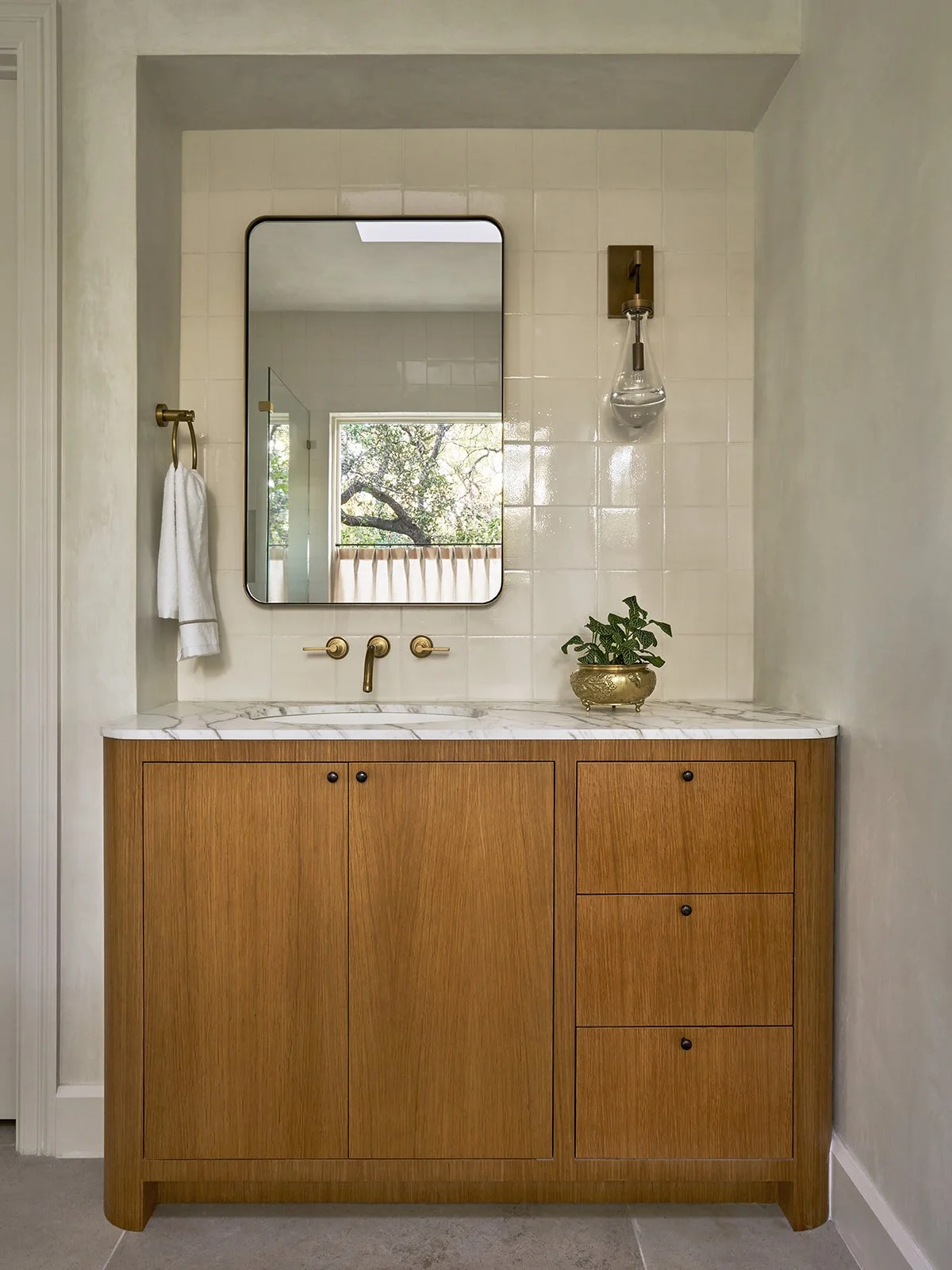 Primary bathroom vanity in an Austin interior design project featuring a custom curved white oak cabinet, marble countertop, metal-framed mirror, and plaster walls styled by Laura Roberts Design.
