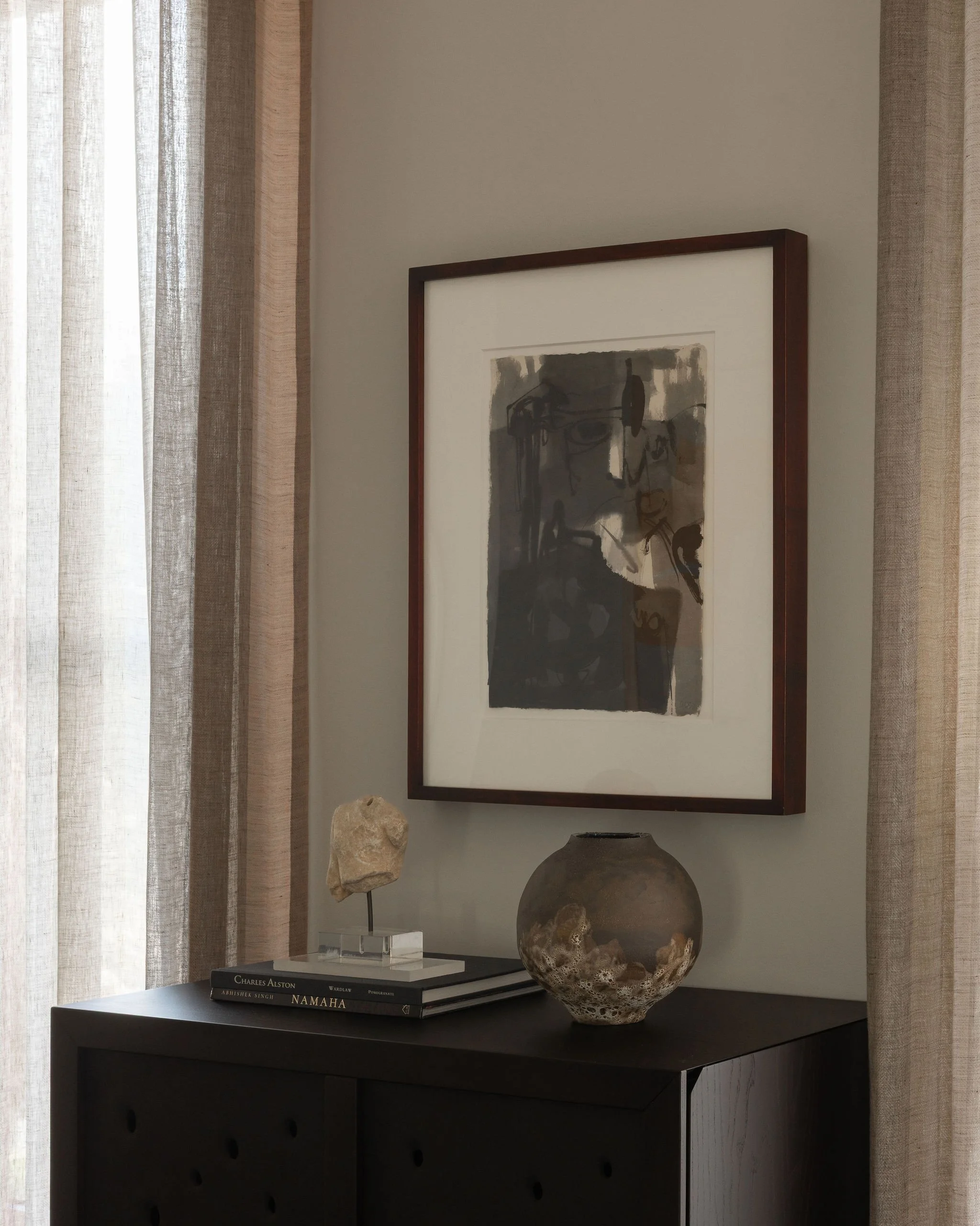 Detail of the living room bar cabinet with a sculptural concrete-paneled finish, abstract artwork by Charles Ainsworth, and a ceramic moon jar by Jane Yang-D’Haene, styled with layered art books and natural textures.