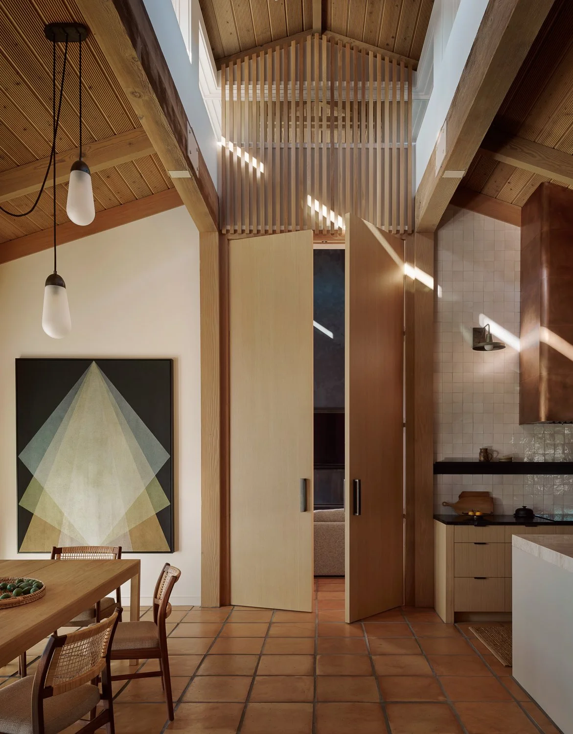 View from the dining room and kitchen toward dramatic full-height white oak doors leading to the family room, anchored by a commissioned Gonzalo Lebrijo painting and a custom white oak dining table.