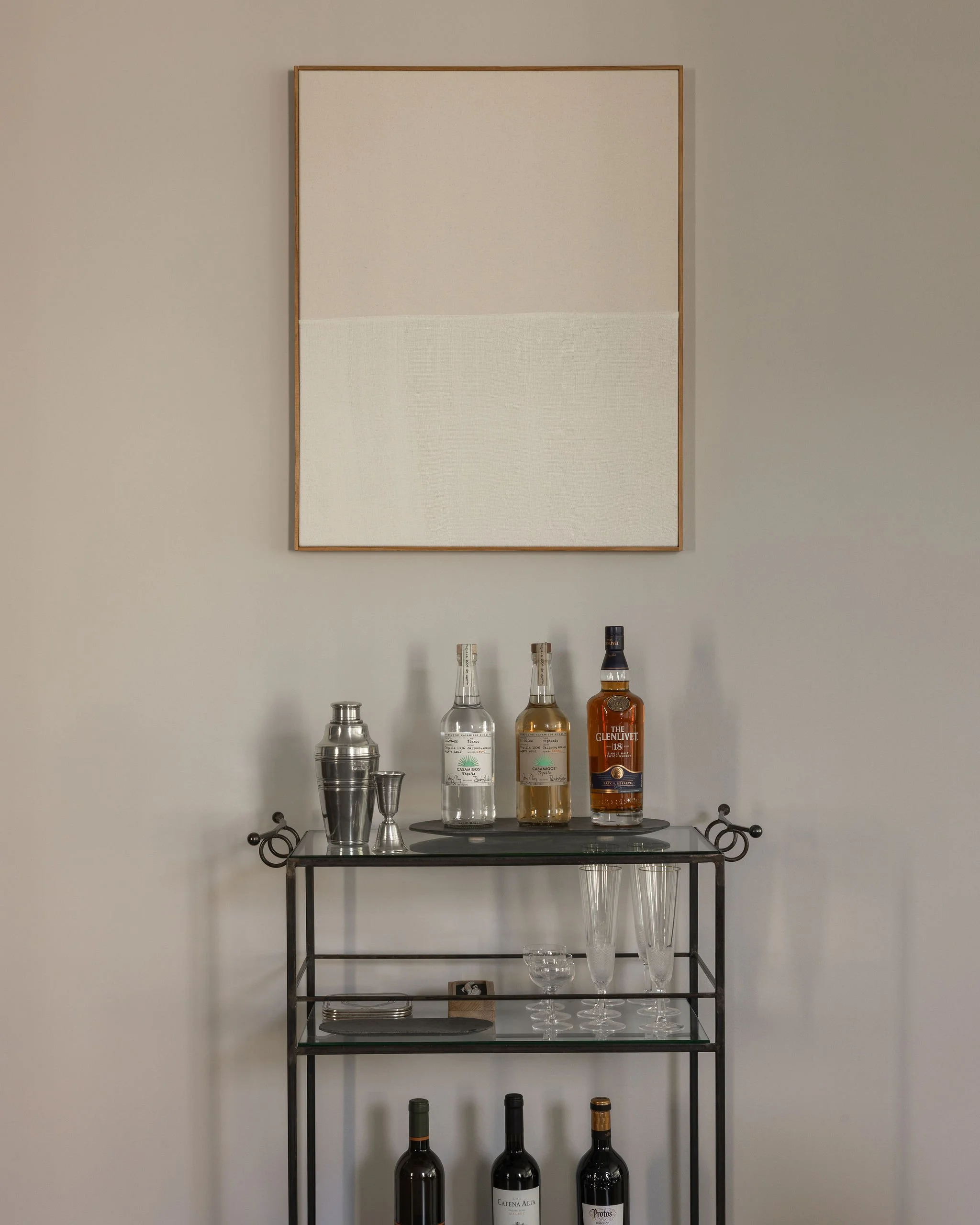 Styled metal and glass bar cart in a Georgetown condo by Austin interior designer Laura Roberts Design, topped with an abstract textile painting by Ethan Cook and curated barware.