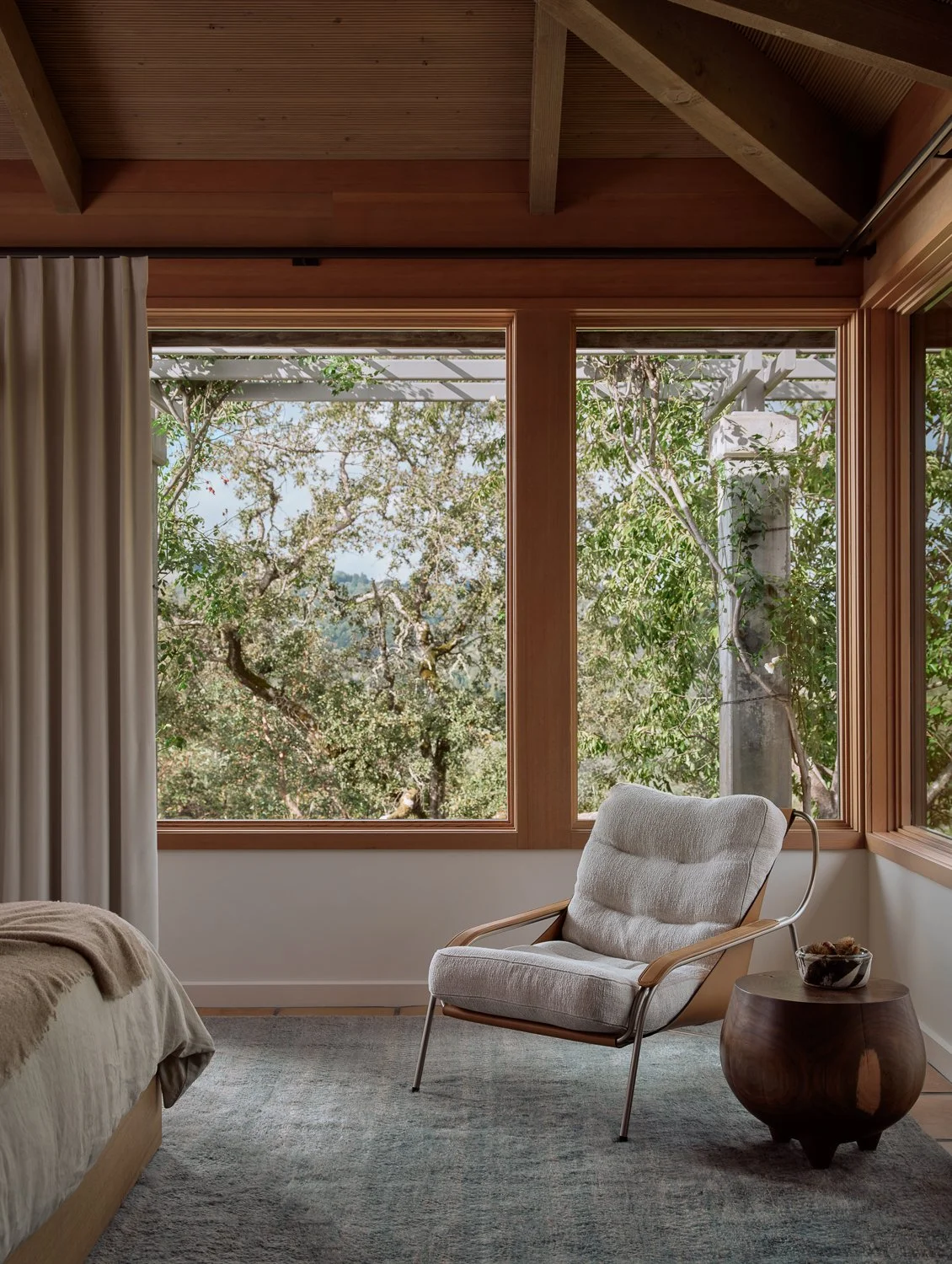 Bedroom seating area with expansive hilltop views, featuring a Zanotta leather and upholstered lounge chair, a sculptural side table by Kieran Kinsella, and windows overlooking the Sonoma landscape.