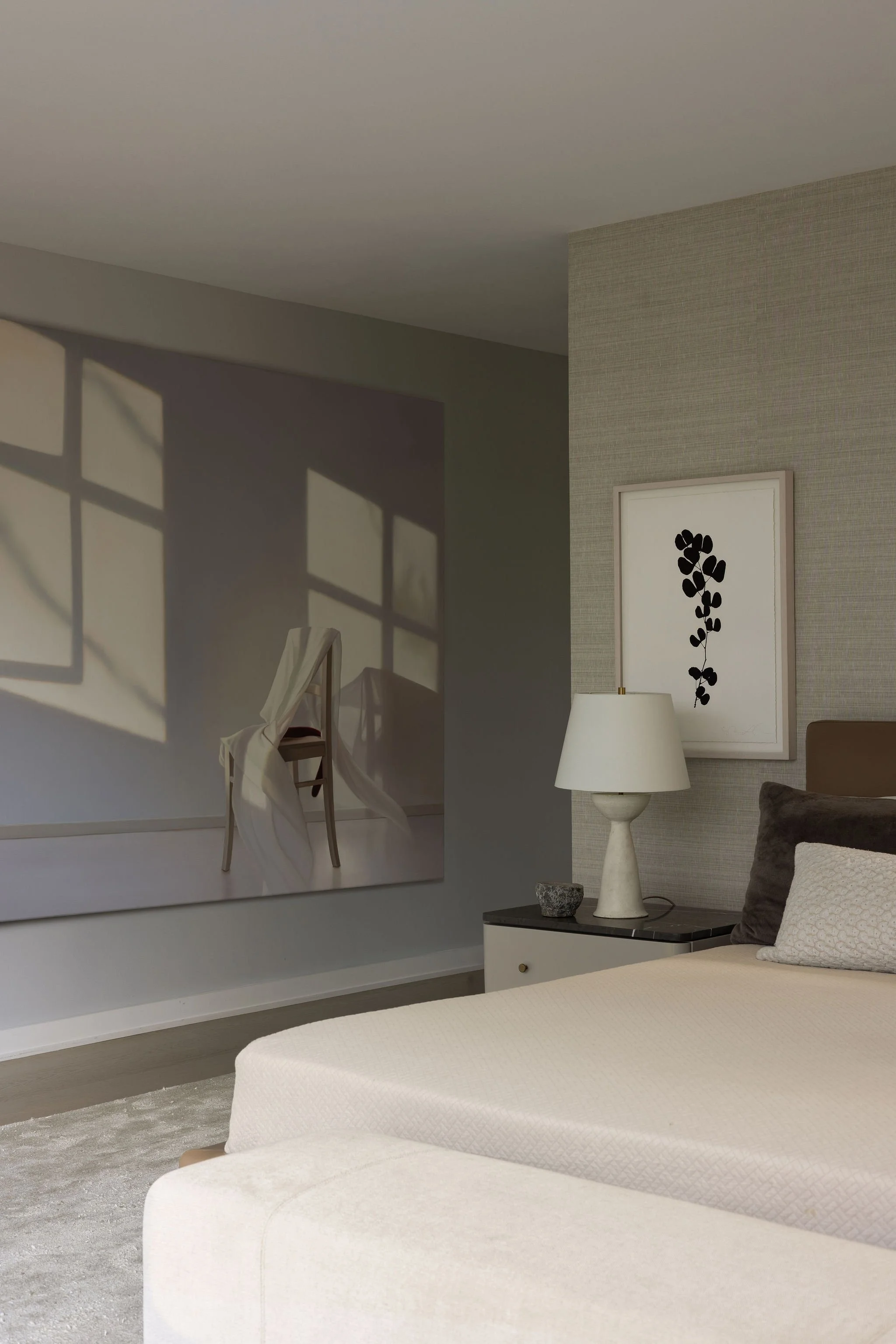 Primary bedroom view by Laura Roberts Design with Minotti bed, plaster lamp, grasscloth wallpaper, and an Edite Grinberga painting creating a window-like effect.