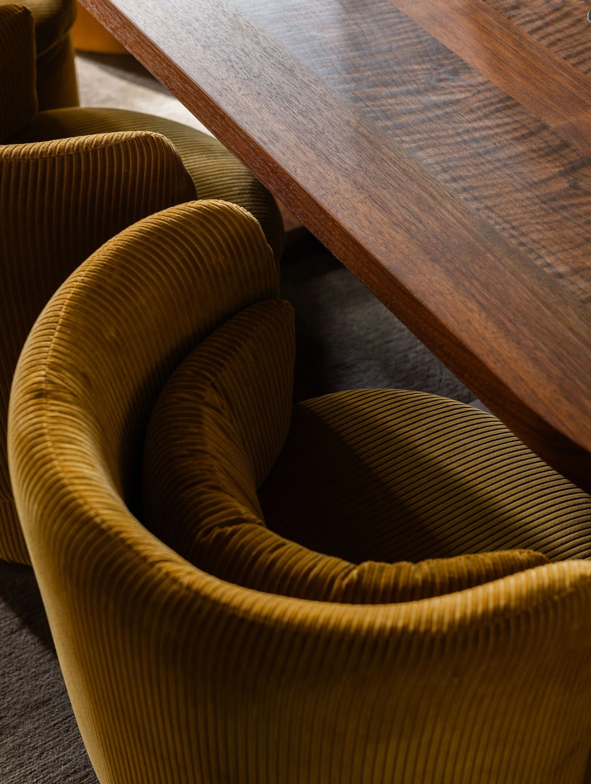 Detail of mustard corduroy upholstered dining chairs with sculptural curves paired with a solid walnut dining table in a McLean, VA home.