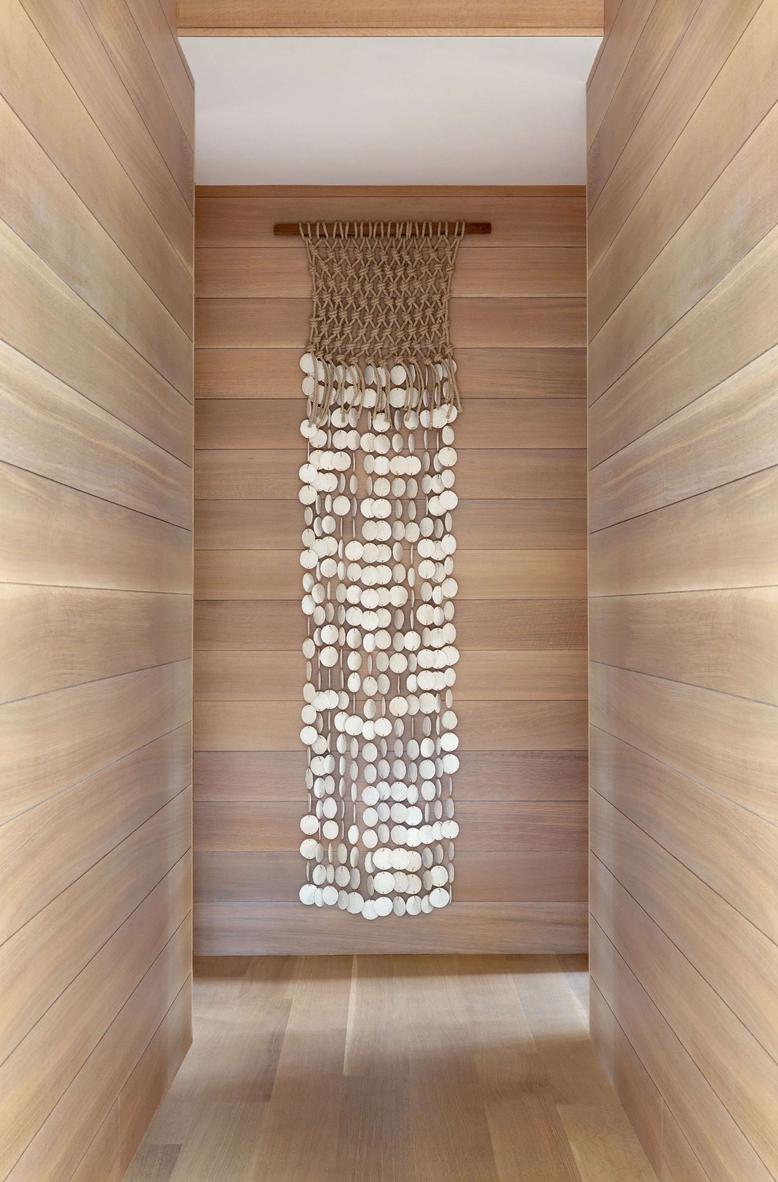 Austin hallway with white oak shiplap walls and floors featuring sculptural macramé and pottery wall art by M Quan.