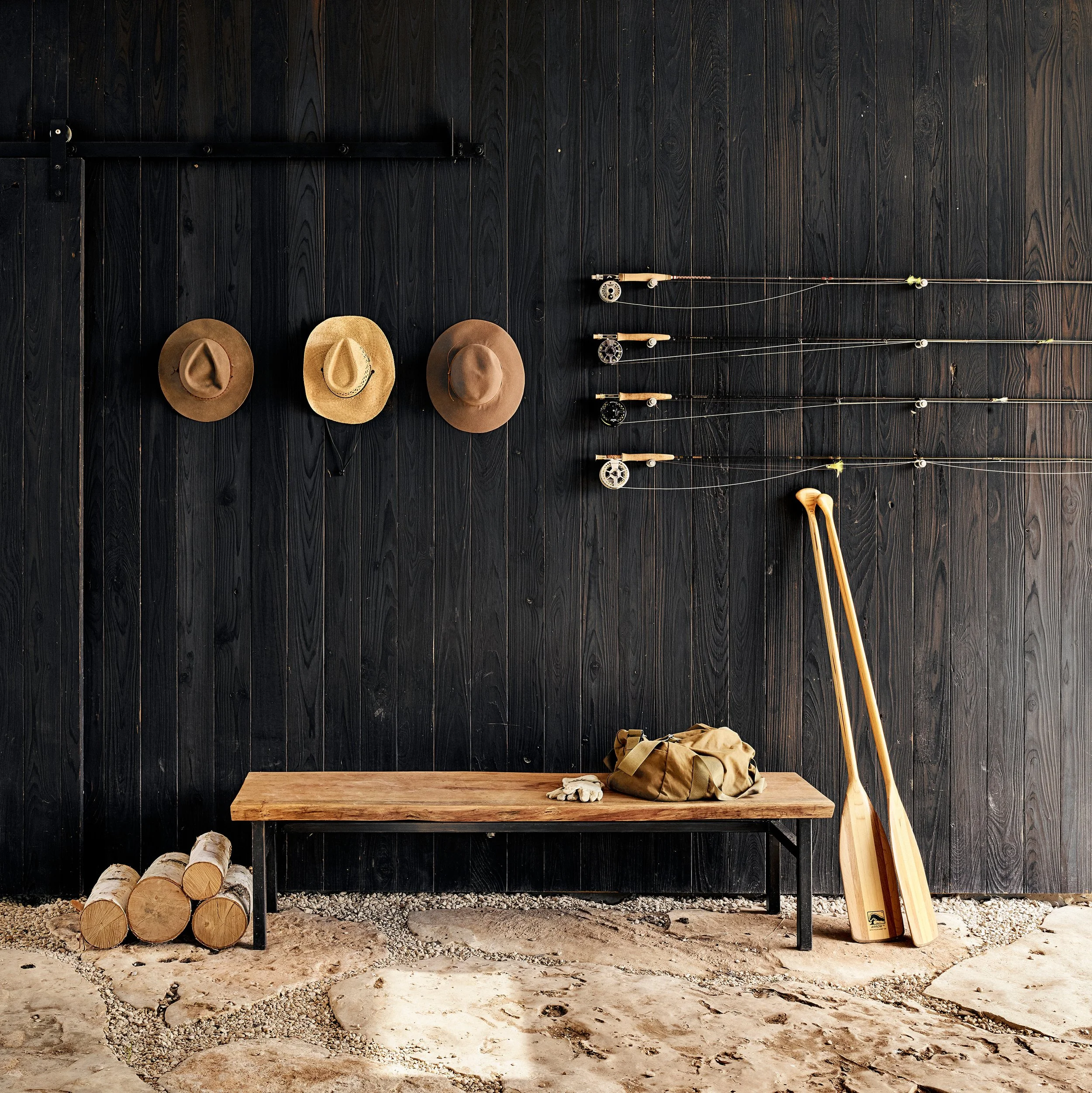 Dogtrot entry of a modern Hill Country home featuring shou sugi ban wood walls, a simple wooden bench, and wall-mounted storage for fly rods and hats.