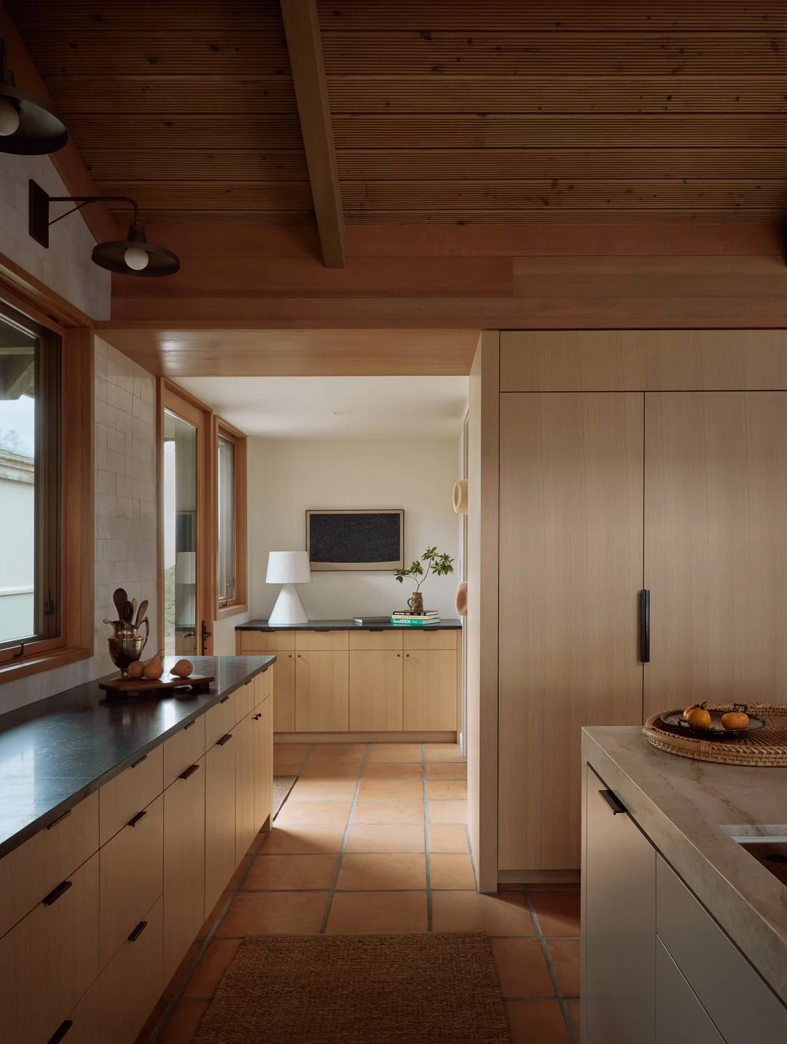 Kitchen view toward the mudroom with custom white oak millwork, soapstone counters, a Rose Uniacke plaster lamp, and artwork by Paul Fägerskiöld.