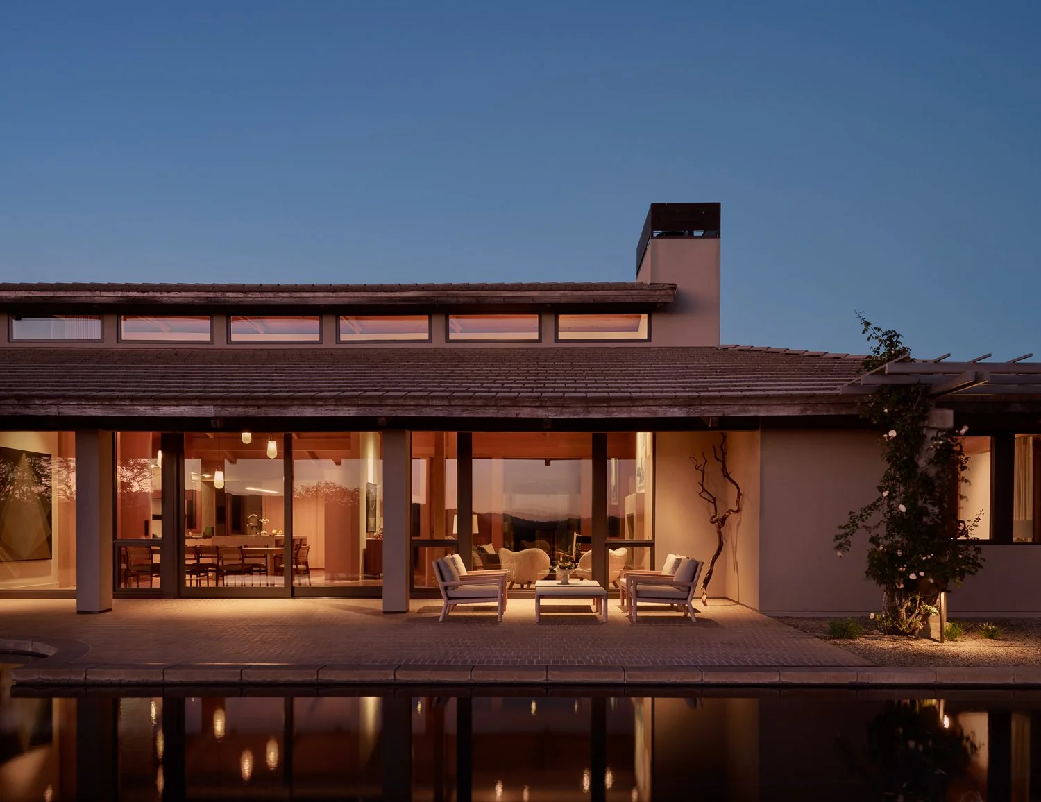Exterior view of a Sonoma wine country residence at dusk, with warm interior light glowing through expansive glass and seamless indoor–outdoor living.