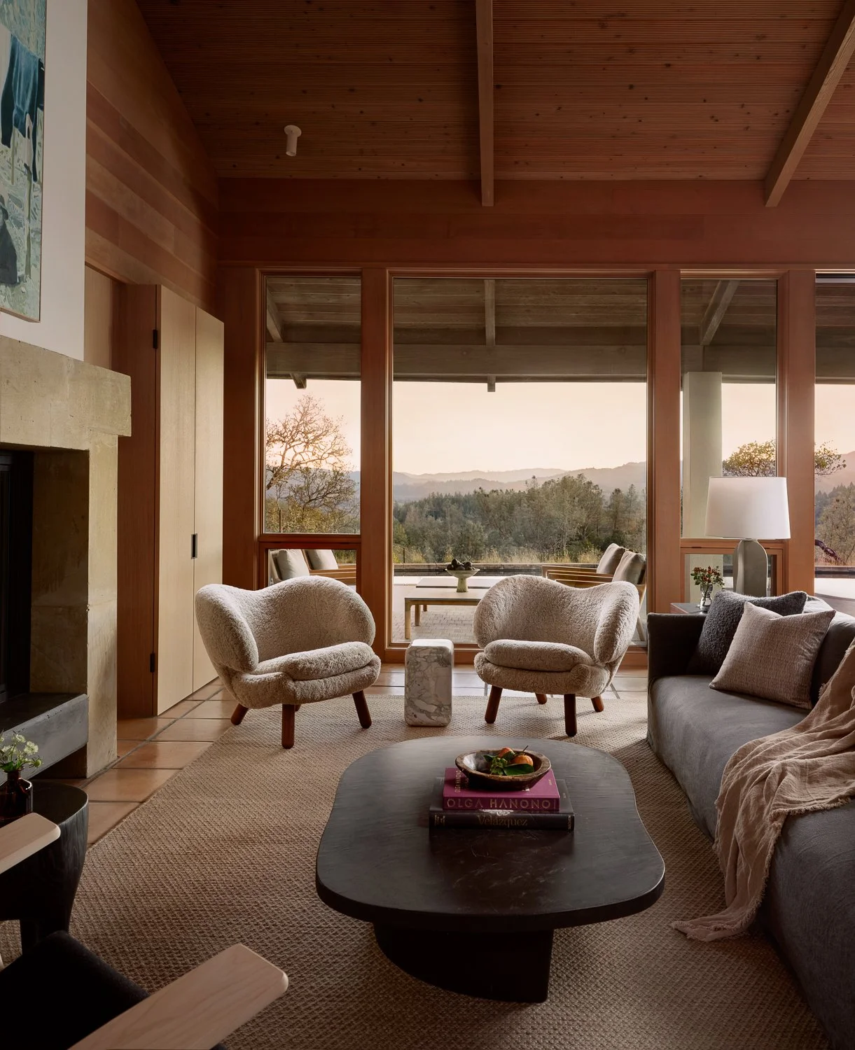 Living room overlooking the Sonoma wine country landscape, featuring a Verellen sofa, Finn Juhl Pelican chairs, a sculptural dark lime plaster coffee table, marble side table, and a closed custom white oak bar cabinet.