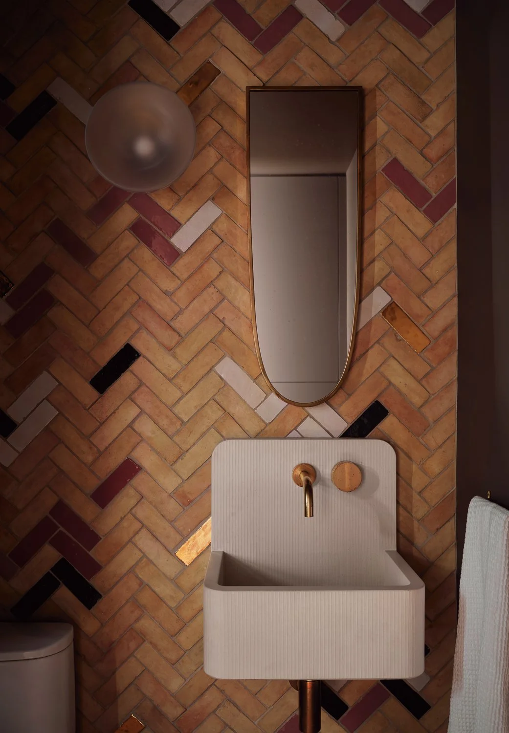Powder room by Laura Roberts Design featuring a herringbone zellige tile feature wall, a wall-hung sink by Kast, and a vintage mirror.
