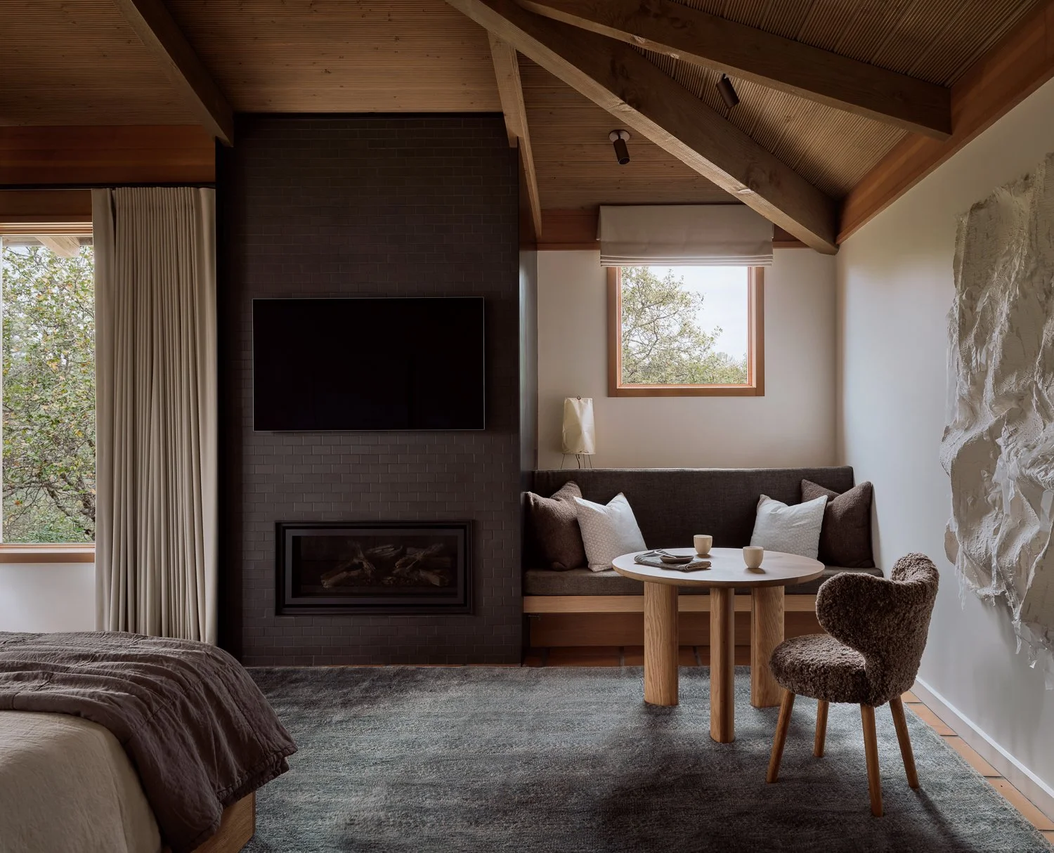 Built-in lounge banquette beside a renovated fireplace clad in Heath Ceramics tile, with a Noguchi lantern and a partial view of the sculptural white silk tapestry by Kenny Nguyen in a Sonoma bedroom.