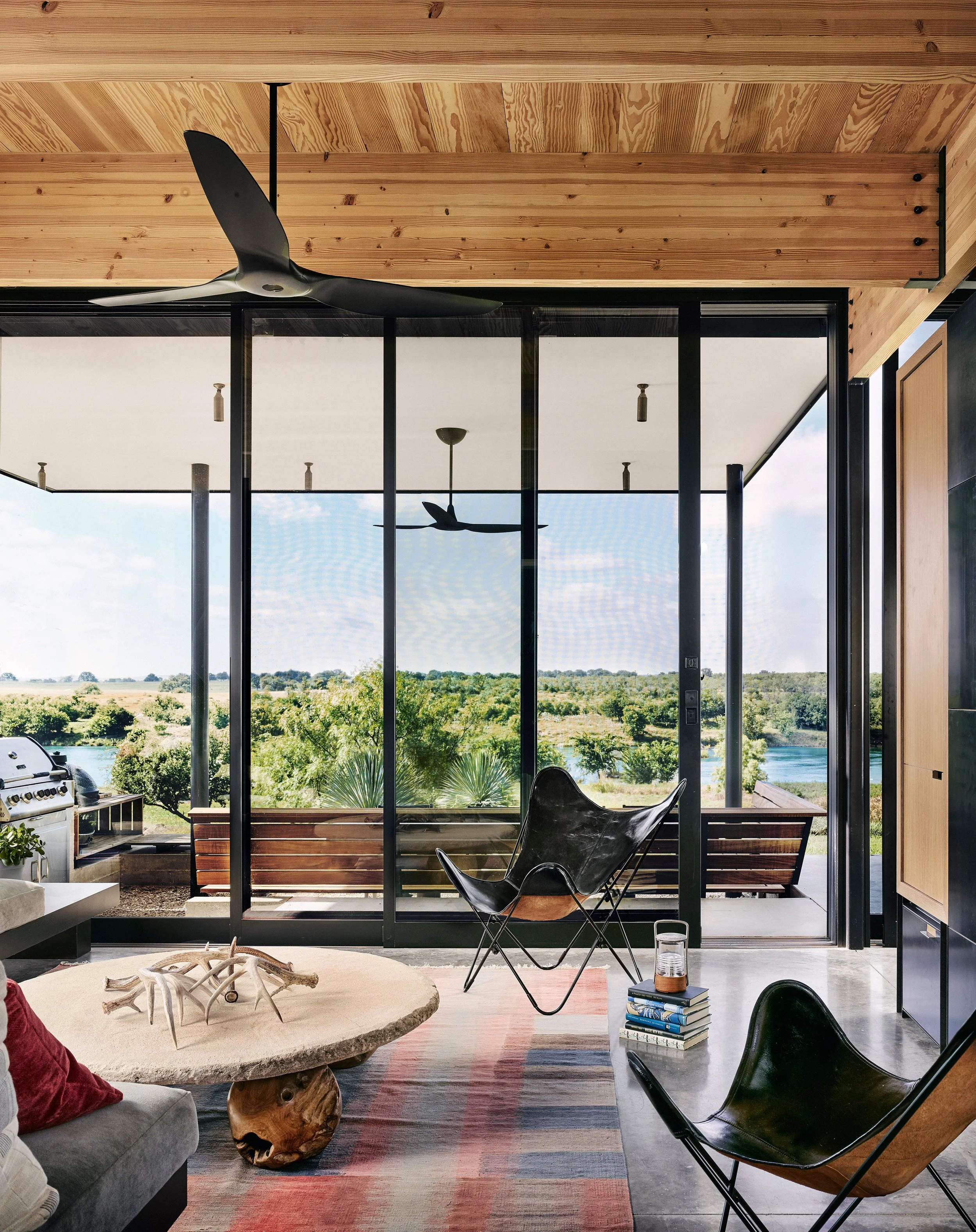 Sitting area off the mudroom featuring a custom stone and wood coffee table, leather butterfly chairs, built-in sectional seating, and expansive views of the Llano River.