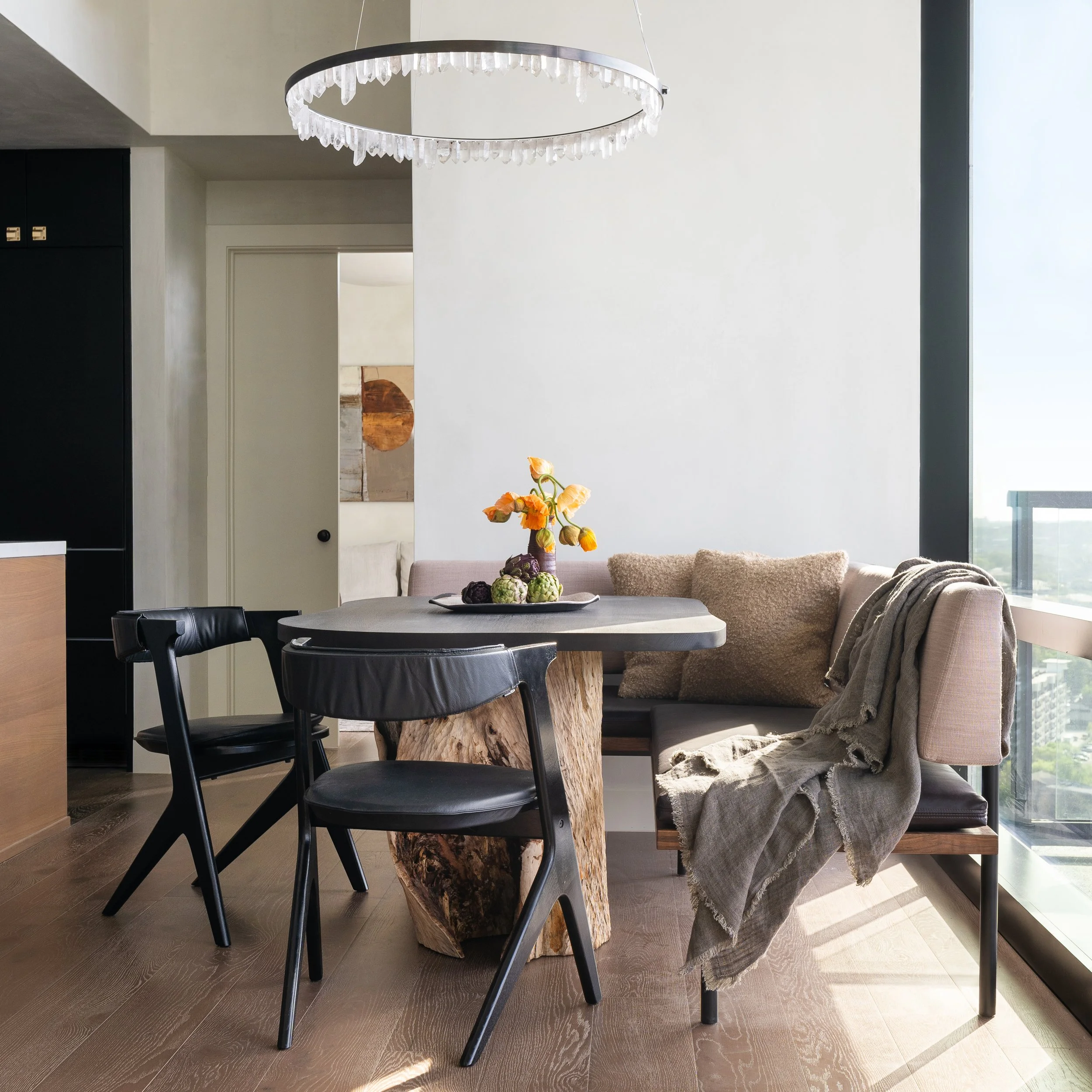 Dining area in a Rainey Street condo with a custom upholstered banquette, sculptural dining table with solid wood pedestal base, and Christopher Boots Prometheus quartz crystal chandelier.