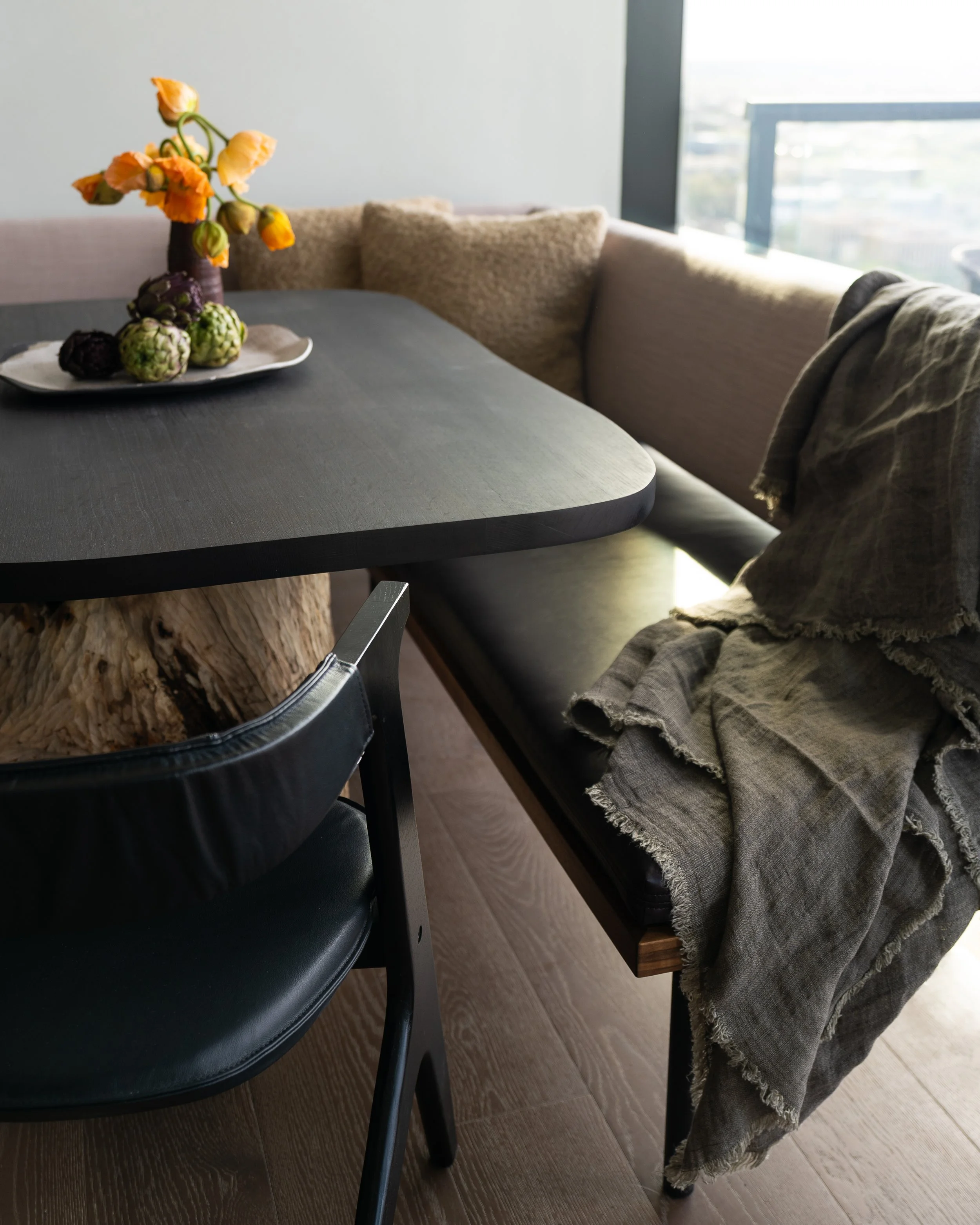 Detail of custom dining table with solid wood pedestal base and minimal upholstered banquette in a Rainey Street condo dining area.