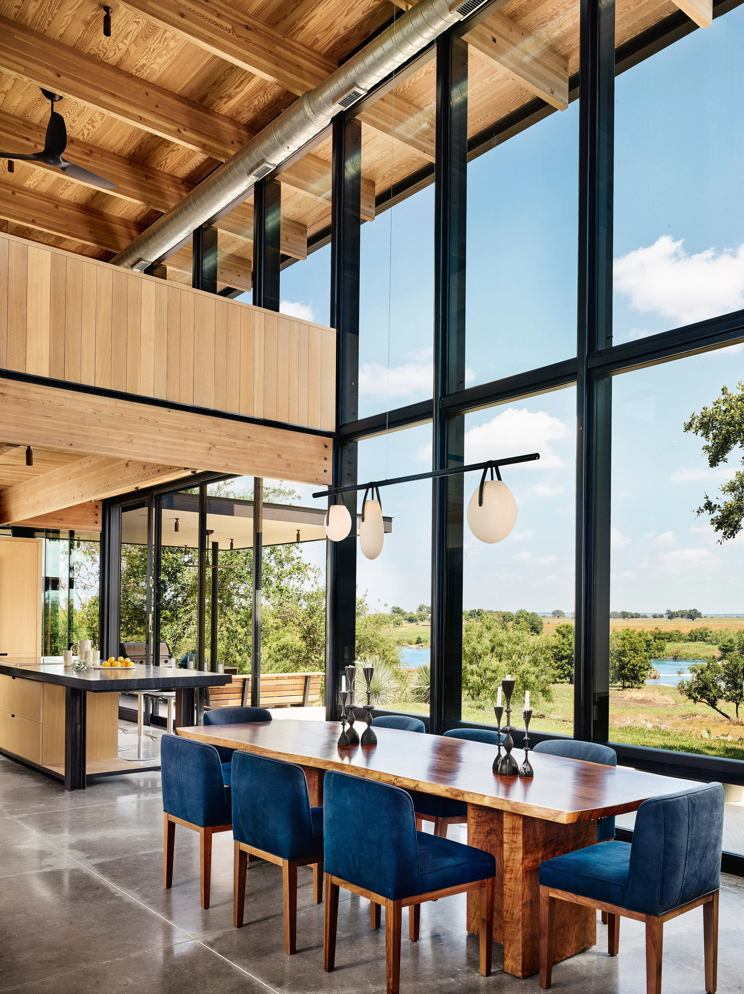 A large custom dining table with Indigo chairs by expansive windows with view of the river.
